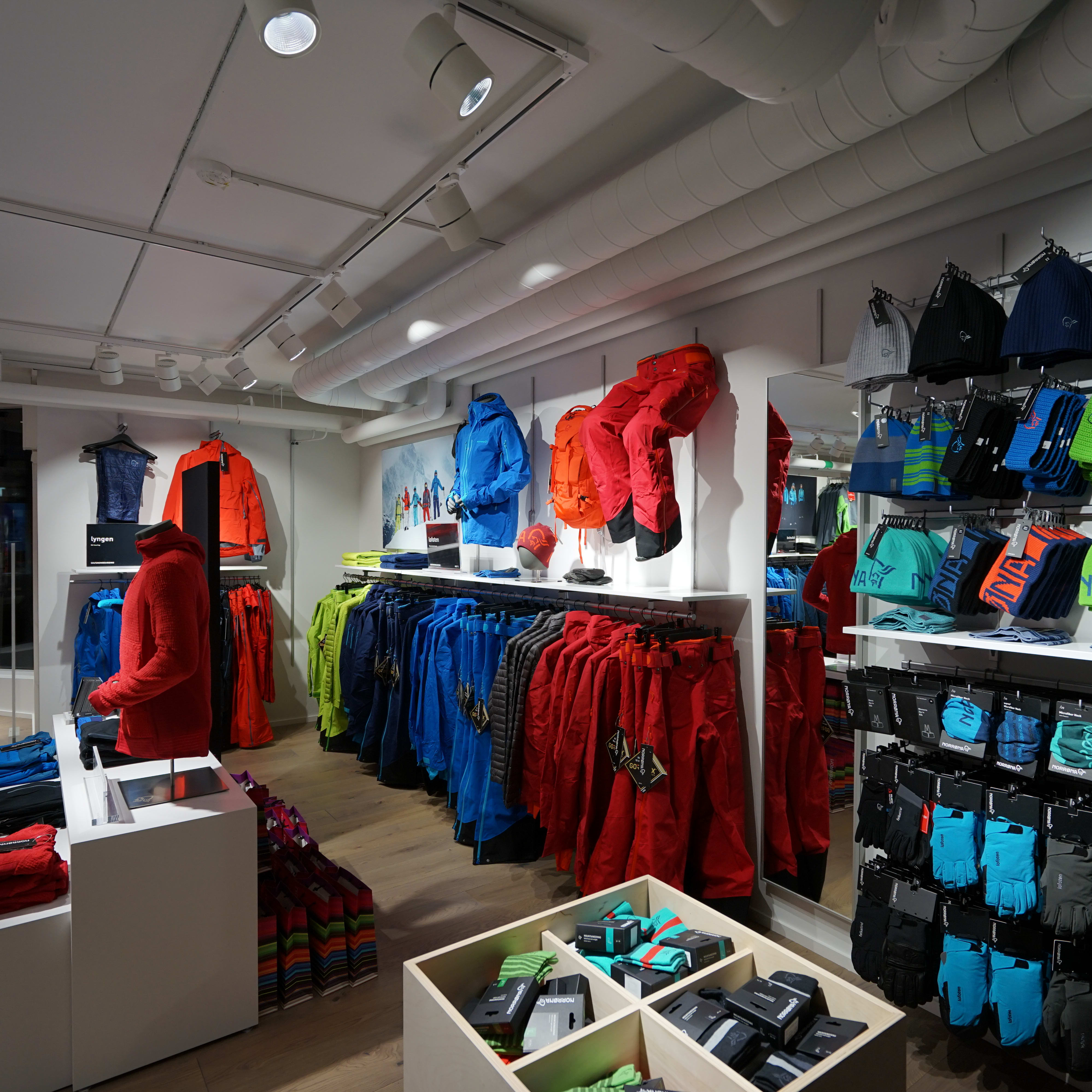 Norrøna retail store displaying colorful outdoor apparel, jackets, pants, beanies, and gloves on racks.