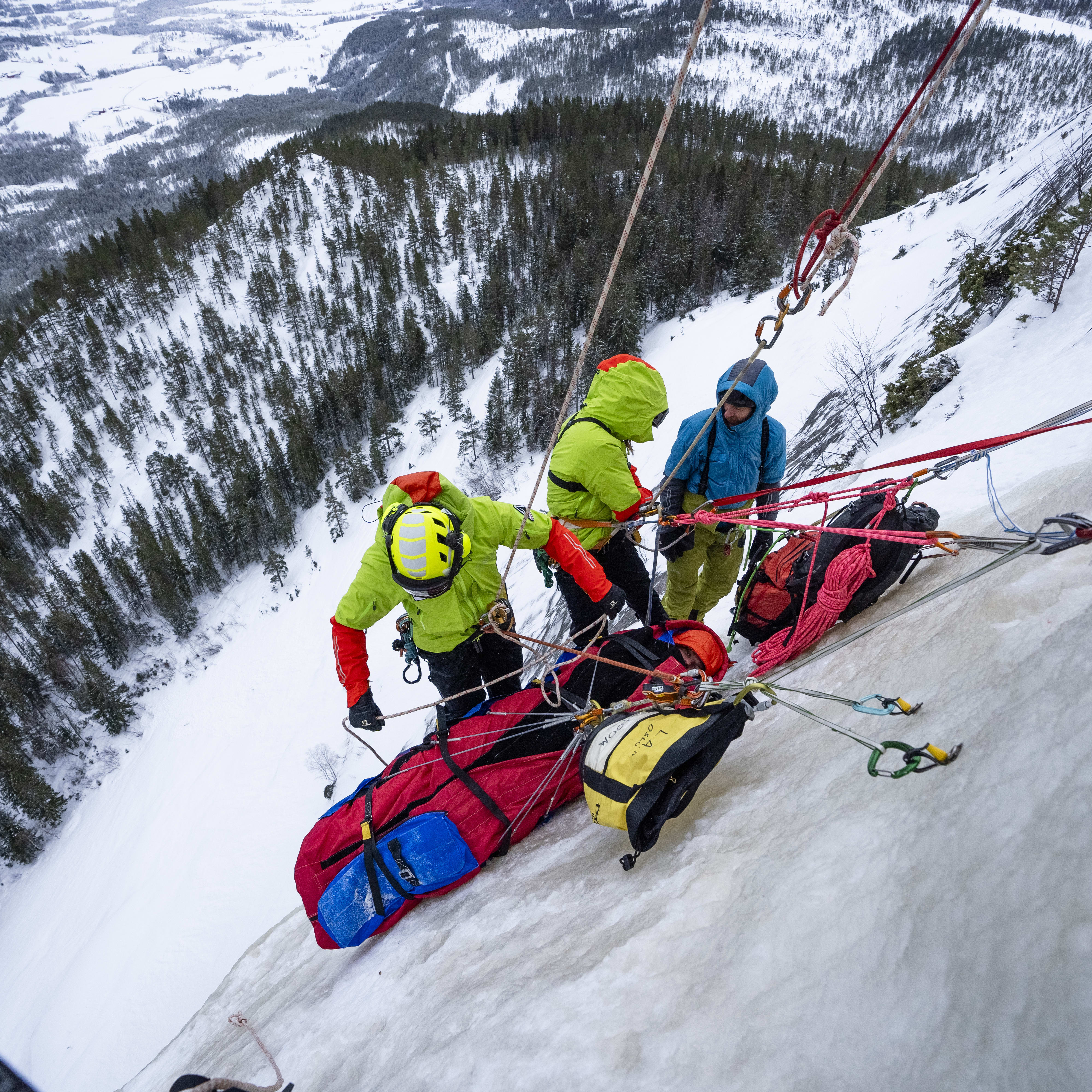 Three climbers on a snowy mountain face.  A climber wearing a yellow Norrøna jacket is rappelling down the ice wall. 
