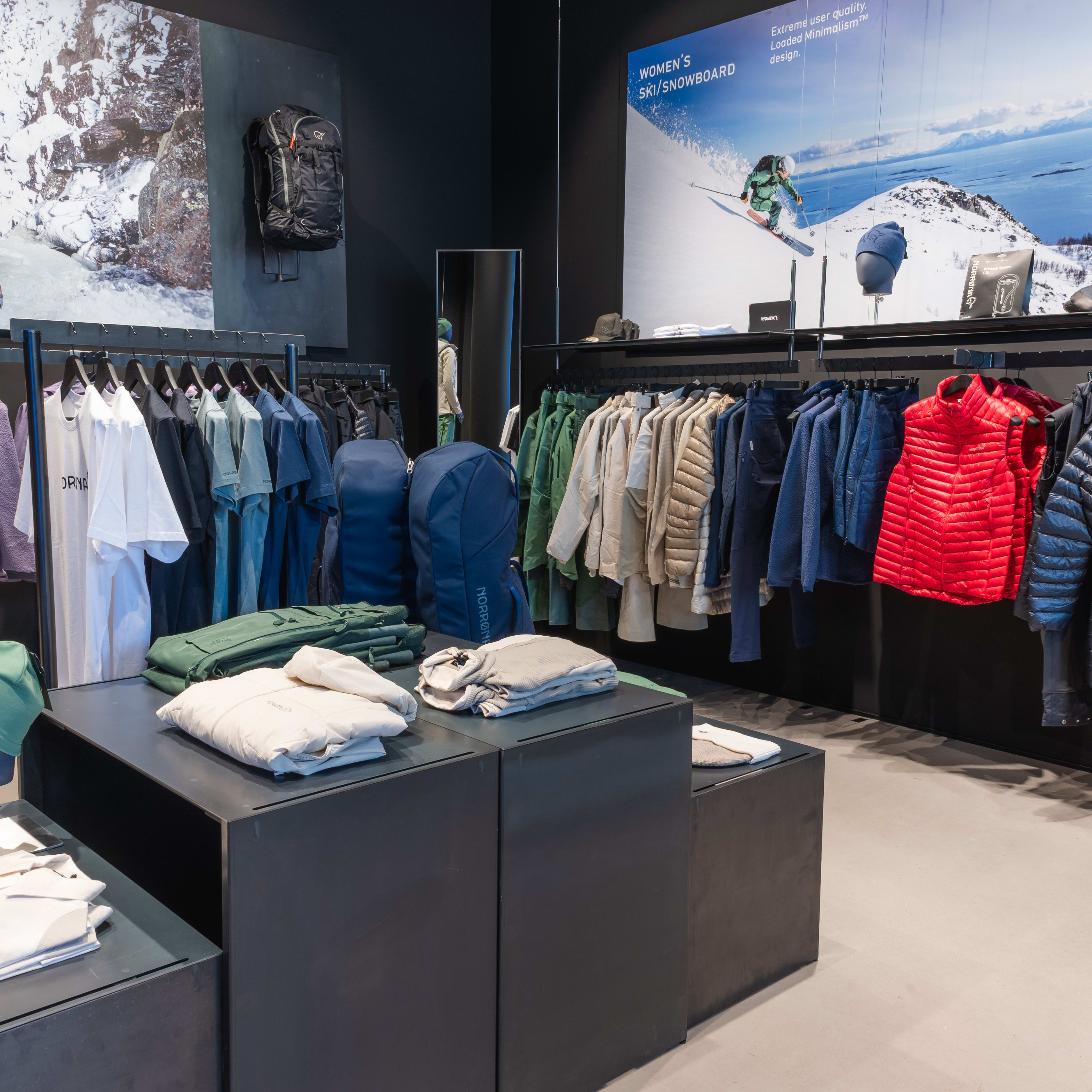 Retail space with Norrøna clothing and gear displayed on racks and tables, featuring action sports imagery in the background.