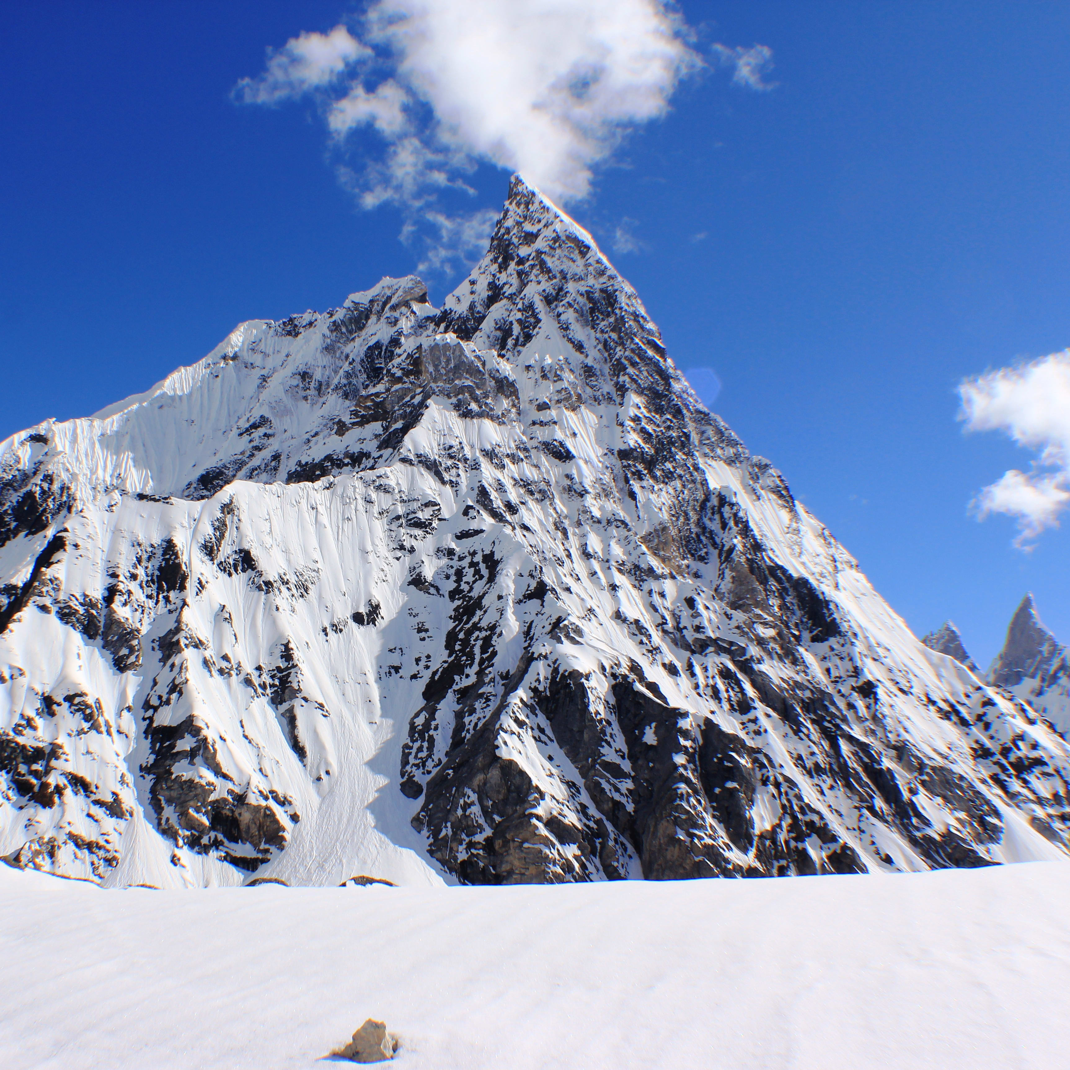 A steep, snow-covered mountain peak against a clear blue sky.