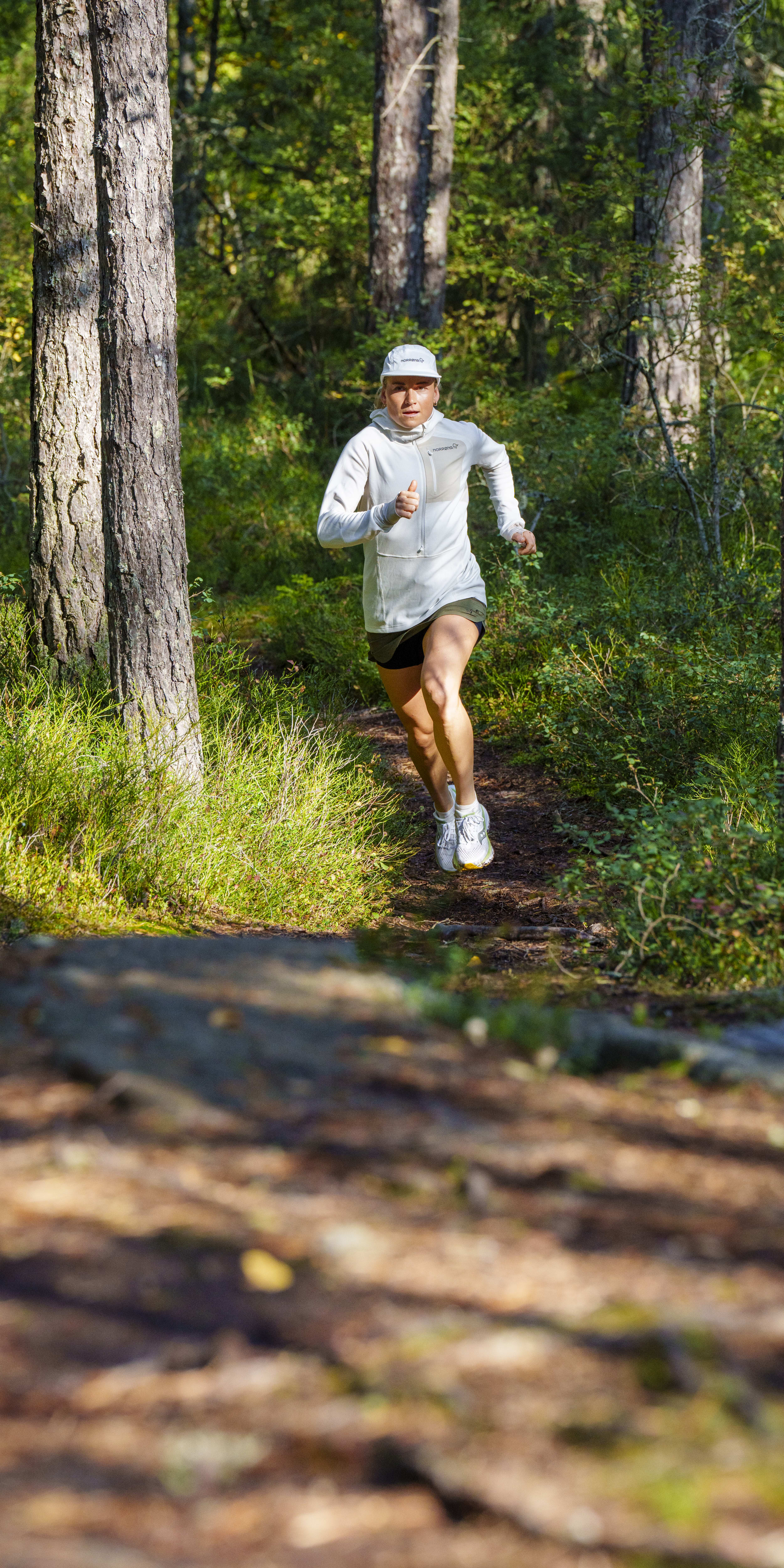A person wearing a Norrøna hoodie runs on a forest path.