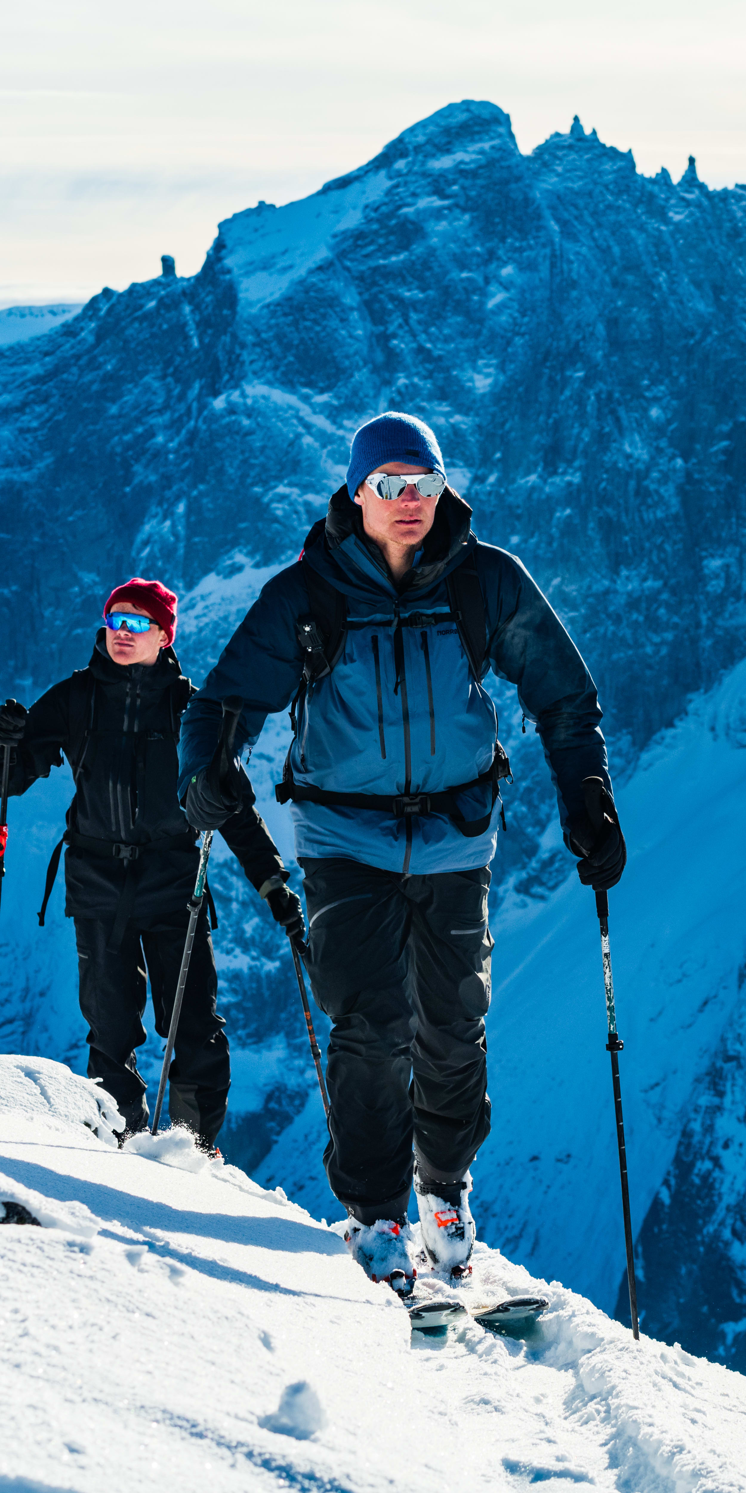 Two skiers in Norrøna gear ascend a snowy mountain range. 
