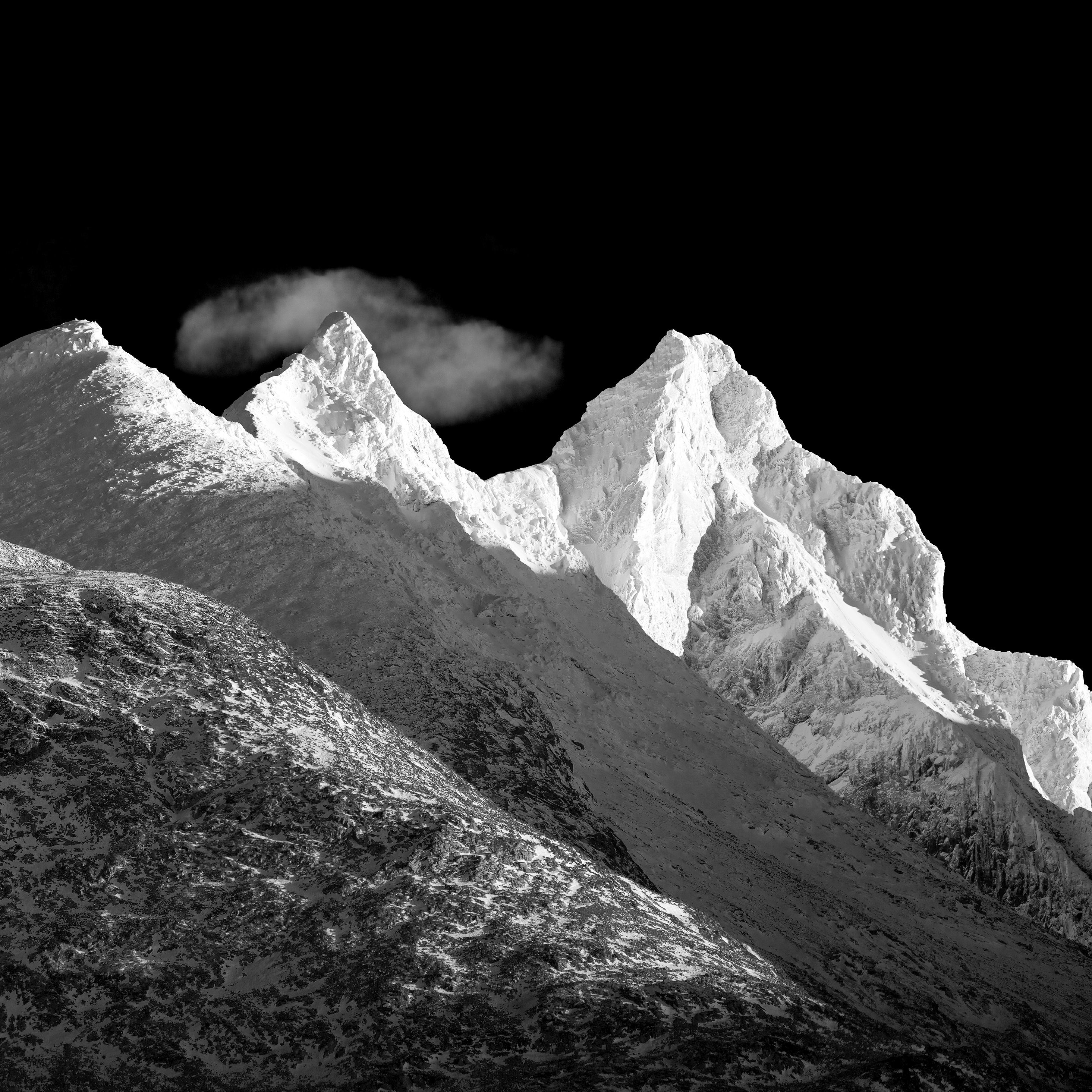 Black and white photo of a snowy mountain range with a cloud covering the peak.