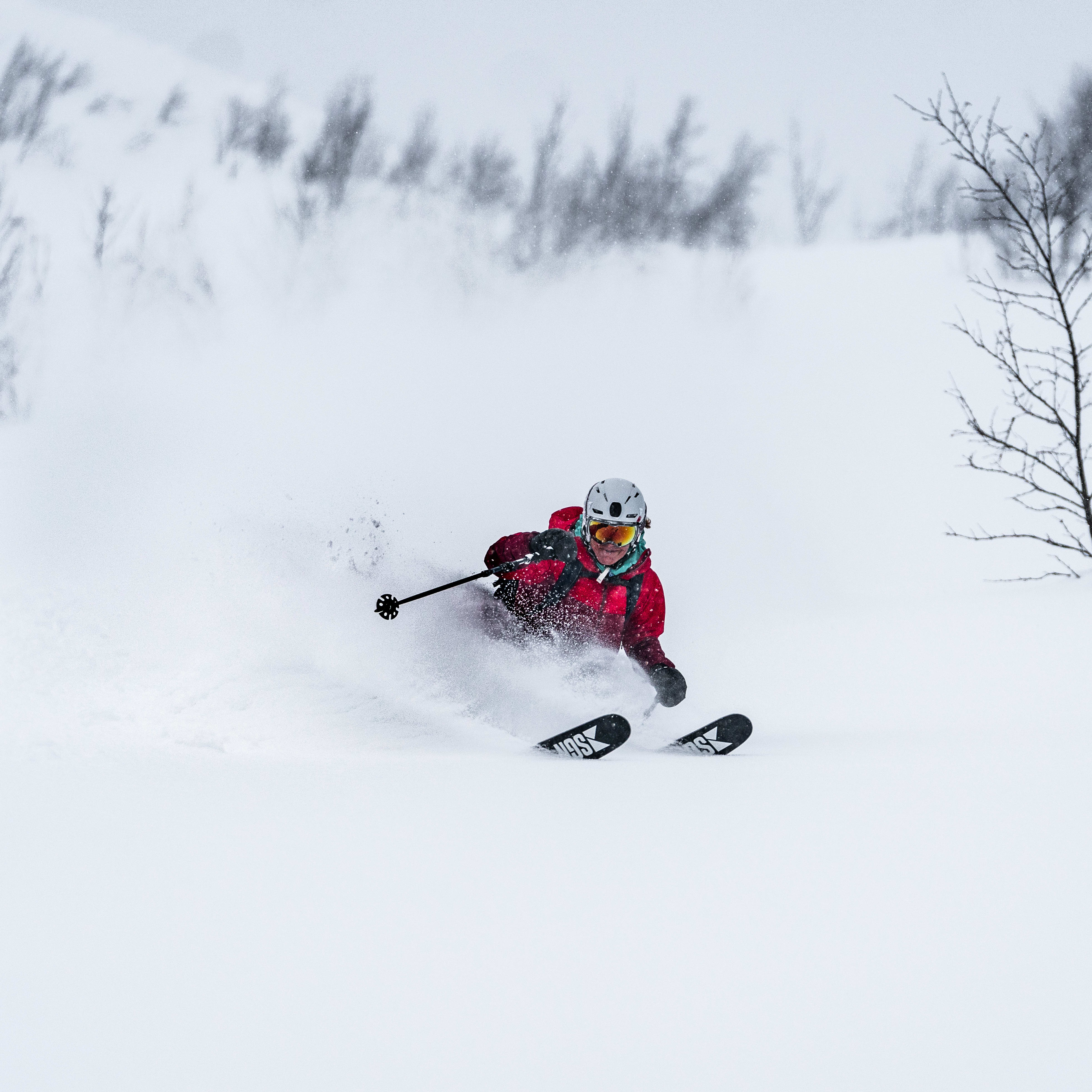 A person wearing a red Norrøna jacket skis down a snowy slope.  
