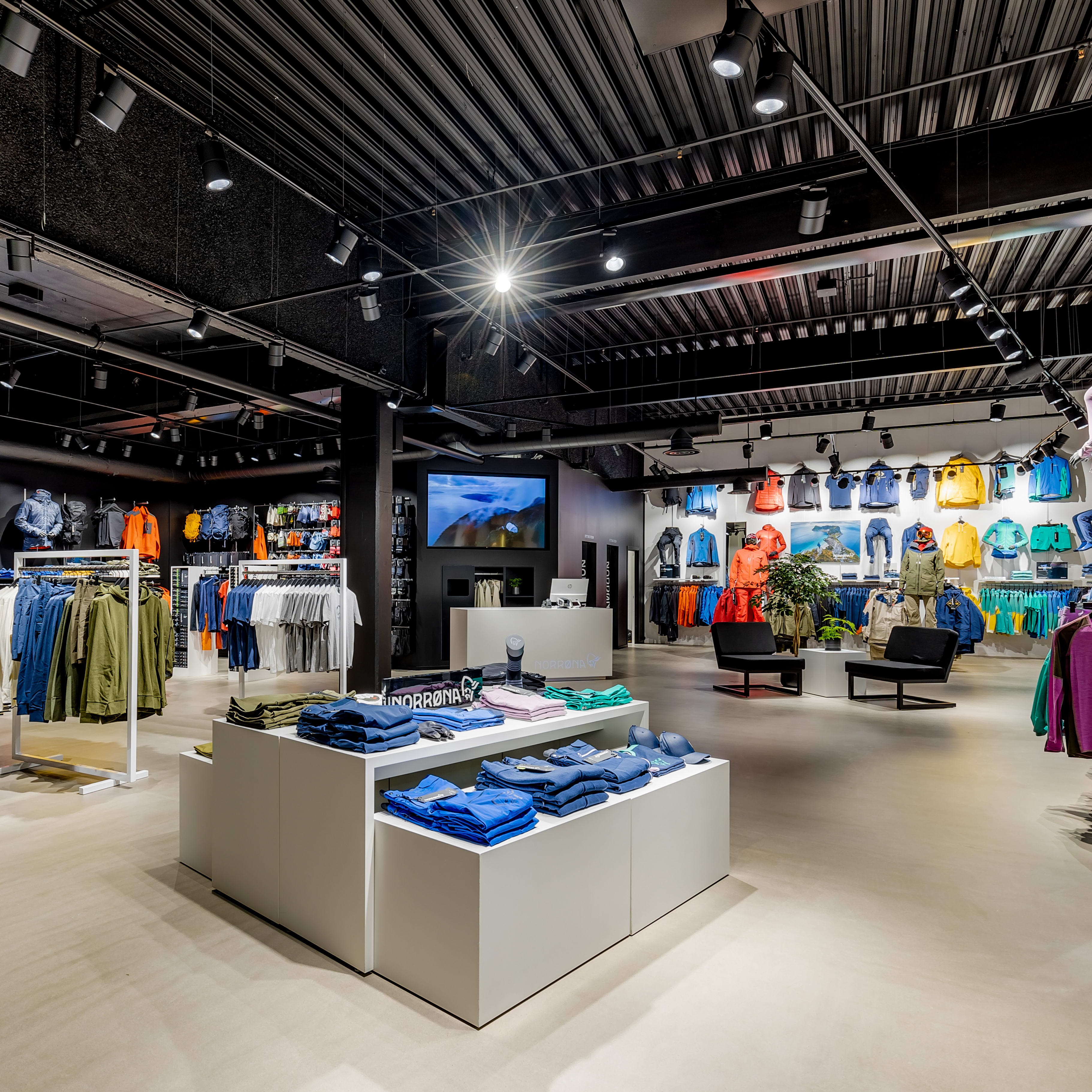 Interior of a modern Norrøna retail store with outdoor clothing on mannequins, racks, and display tables.