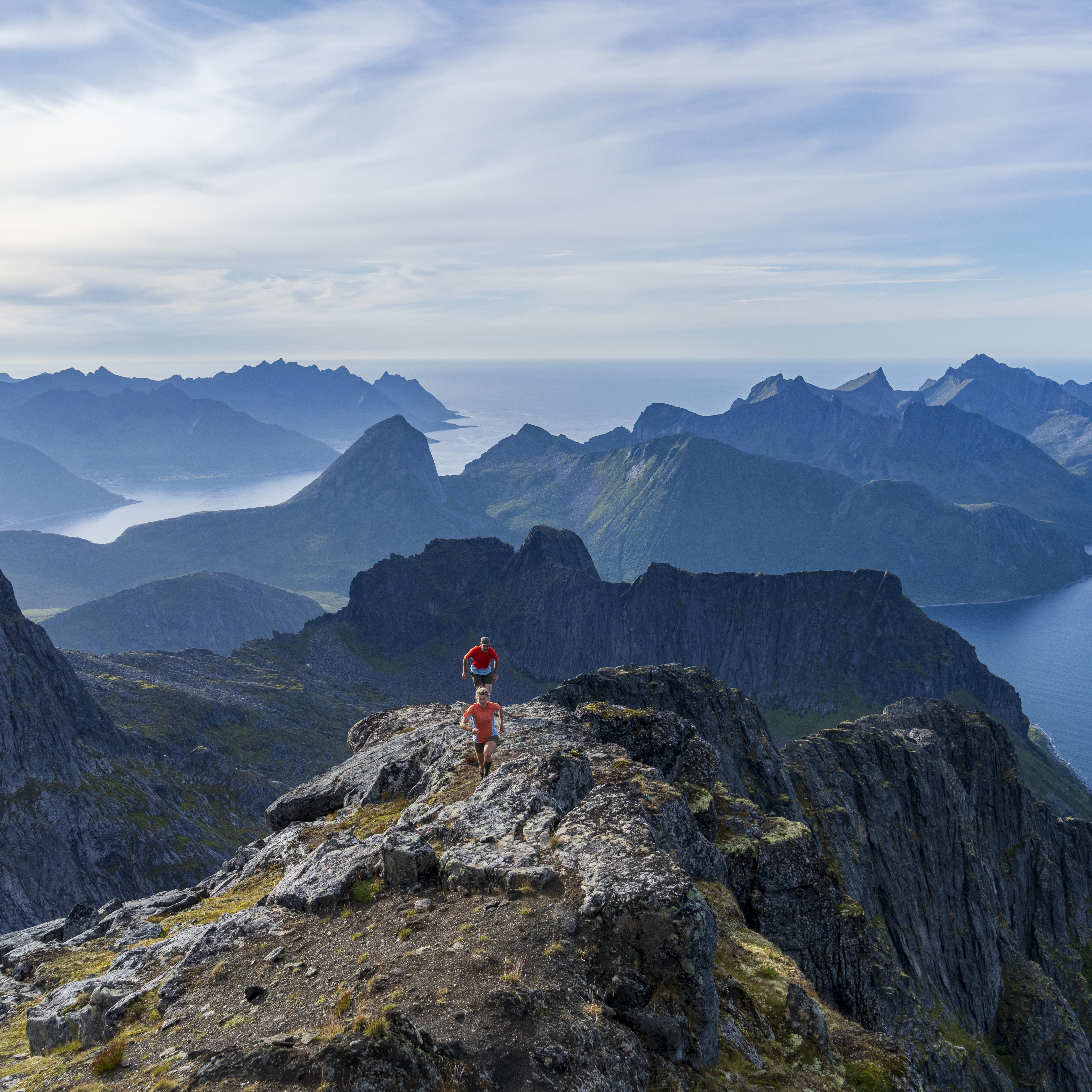 Two people hiking on a rocky mountain ridge overlooking the ocean. 
