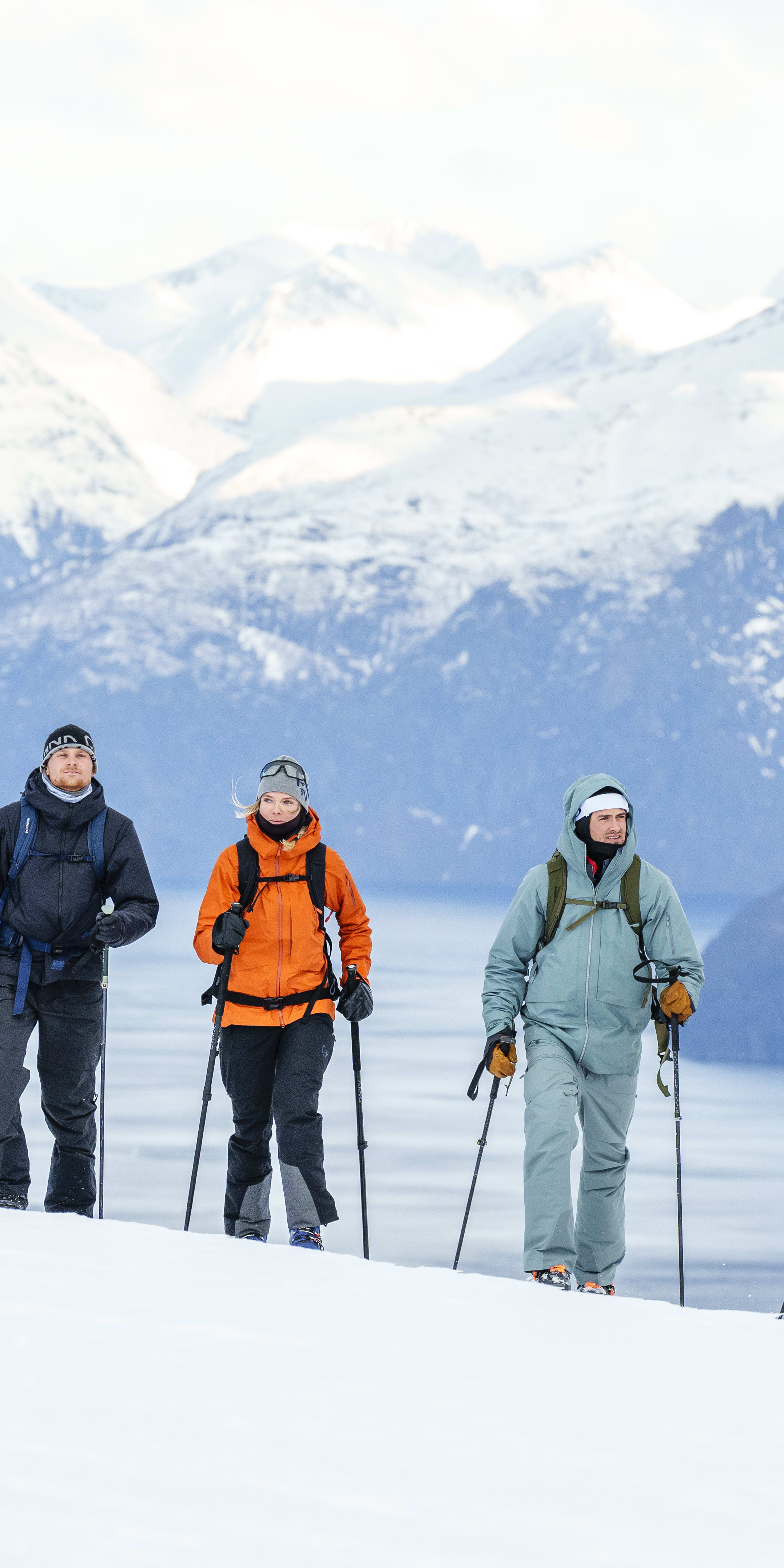 Five people wearing Norrøna clothing are backcountry skiing in a snowy mountain landscape. 

