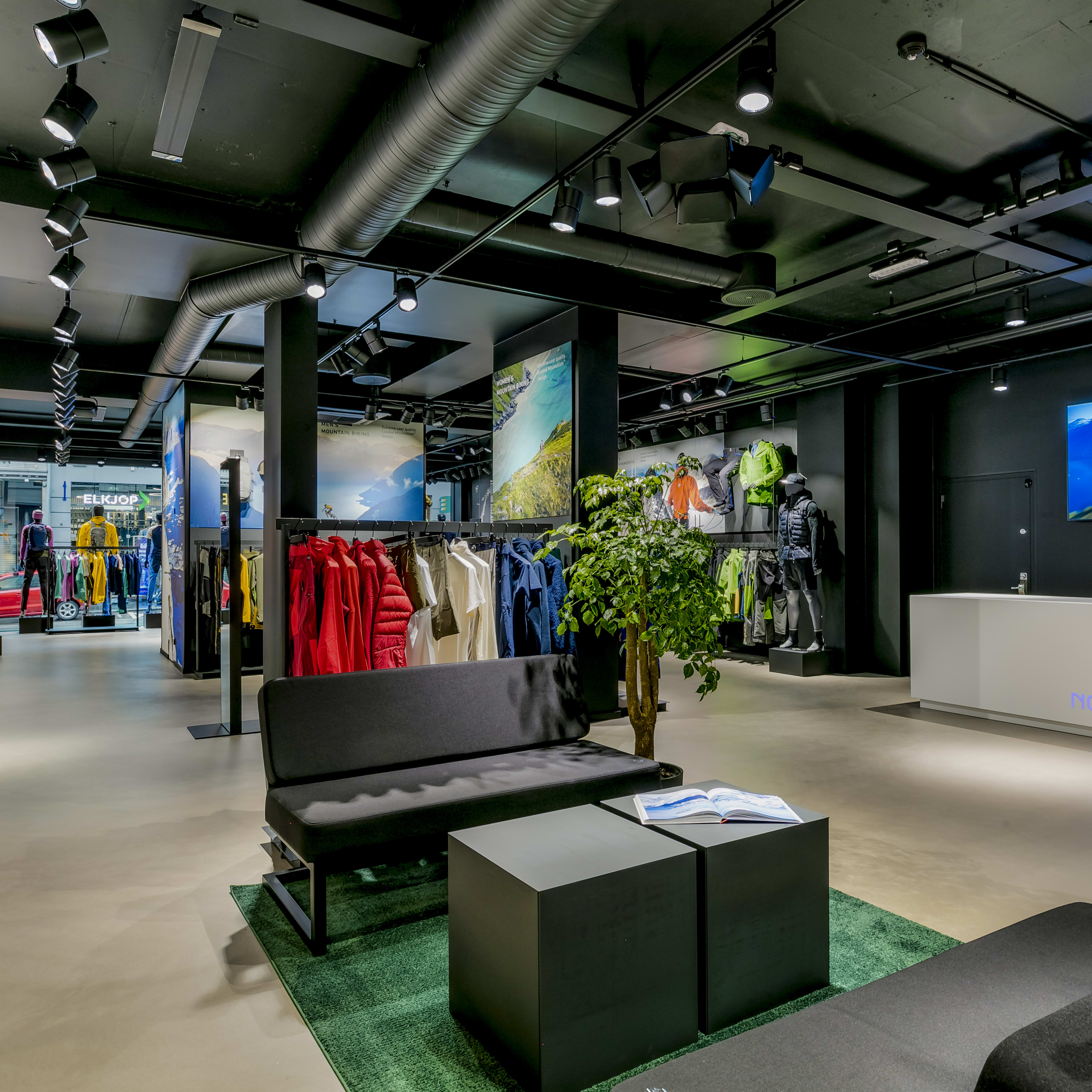 Norrøna clothing store interior featuring outdoor apparel displays, a seating area, and a checkout counter.