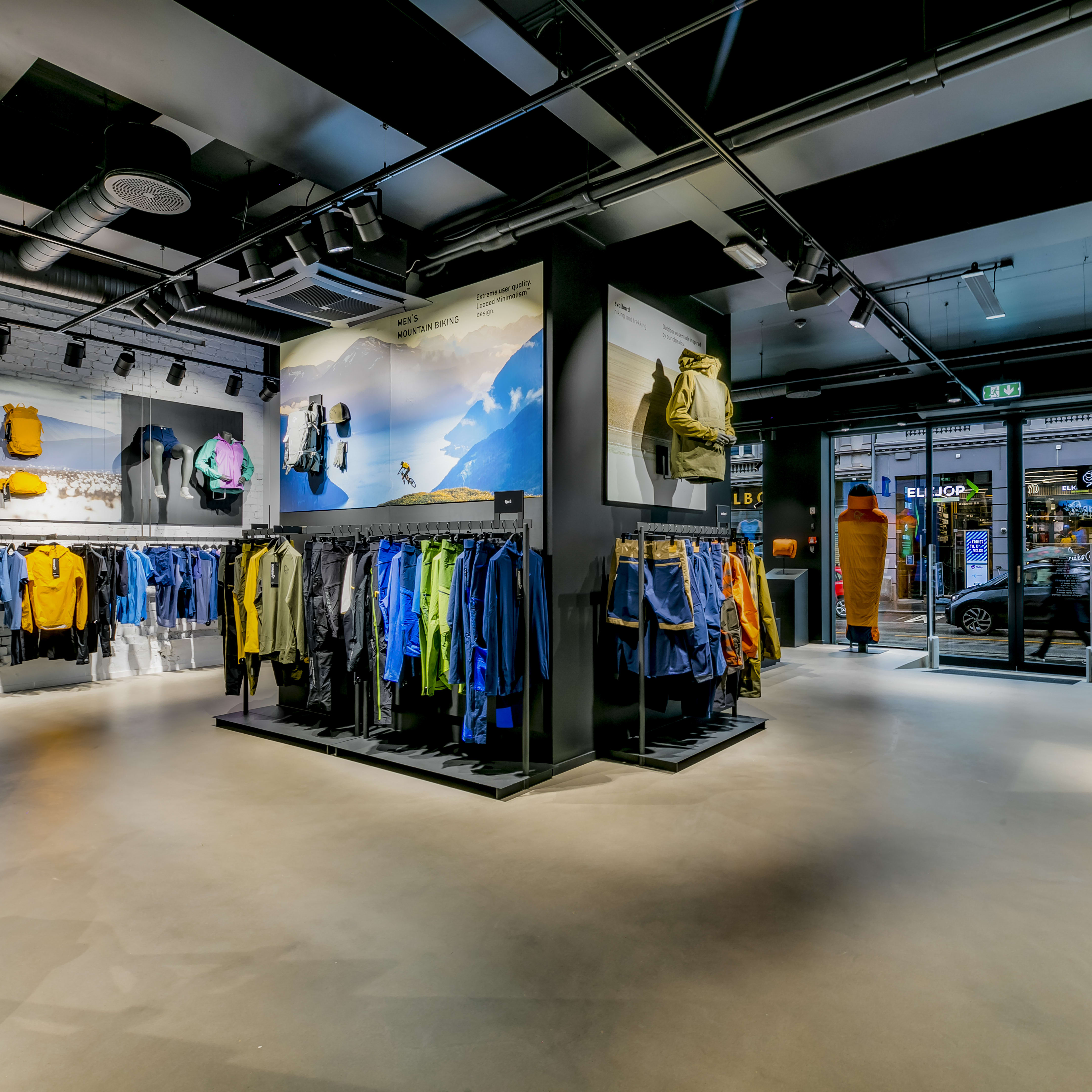 Modern Norrøna store interior with colorful outdoor clothing on racks and scenic wall displays.