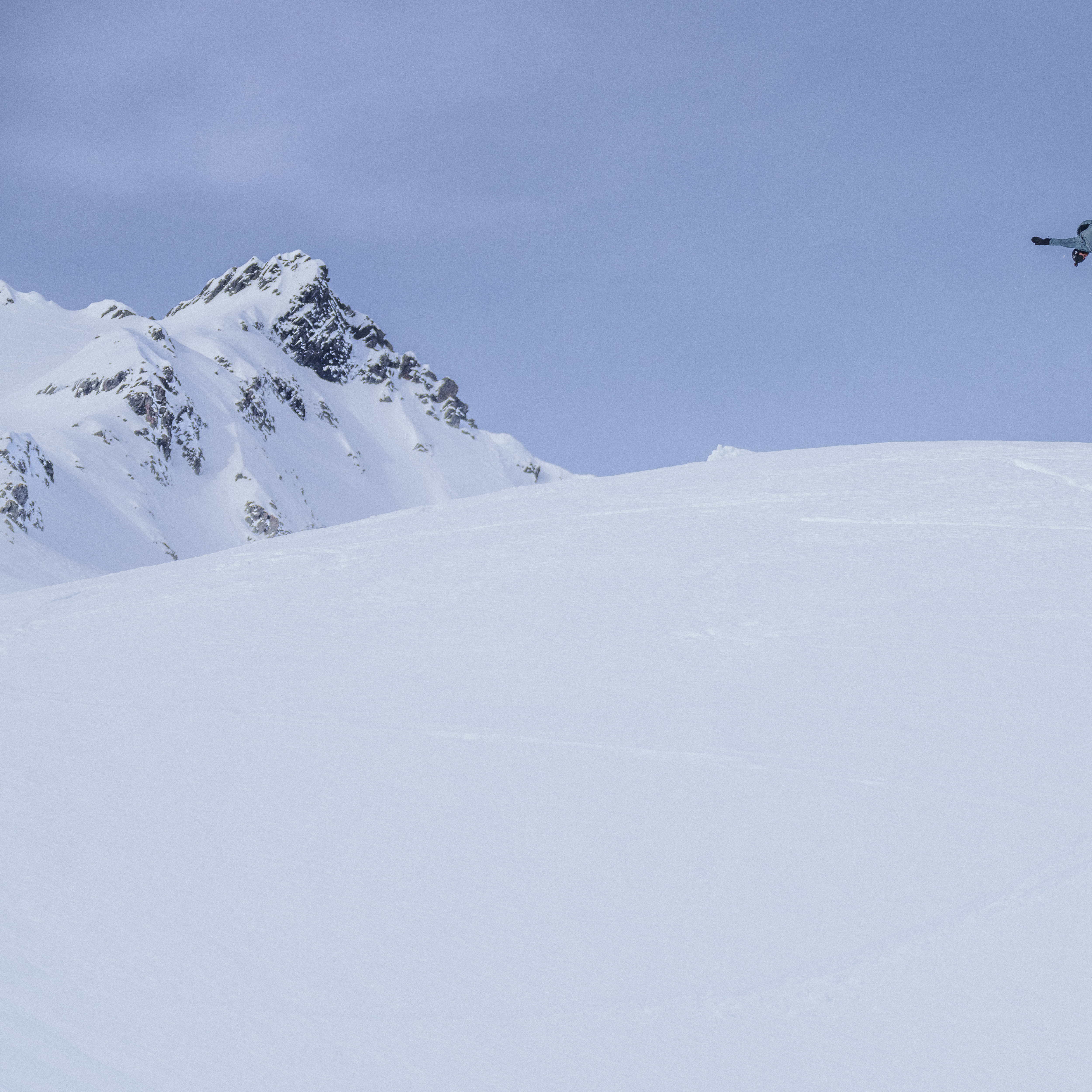 A snowboarder in a Norrøna jacket performs a trick in the air over a snowy mountain. 
