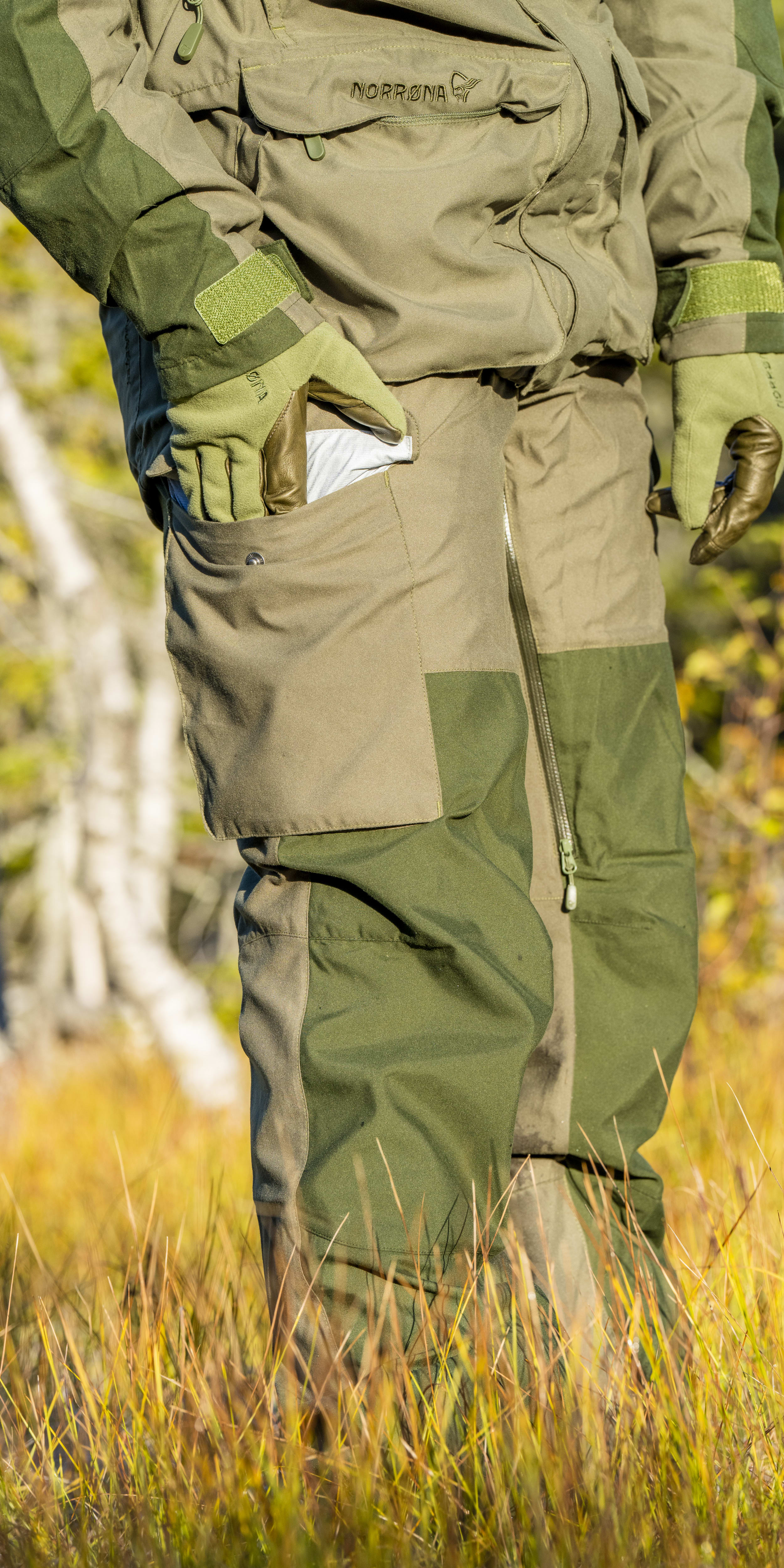 A person wearing a pair of Norrøna green pants is standing in tall grass. 
