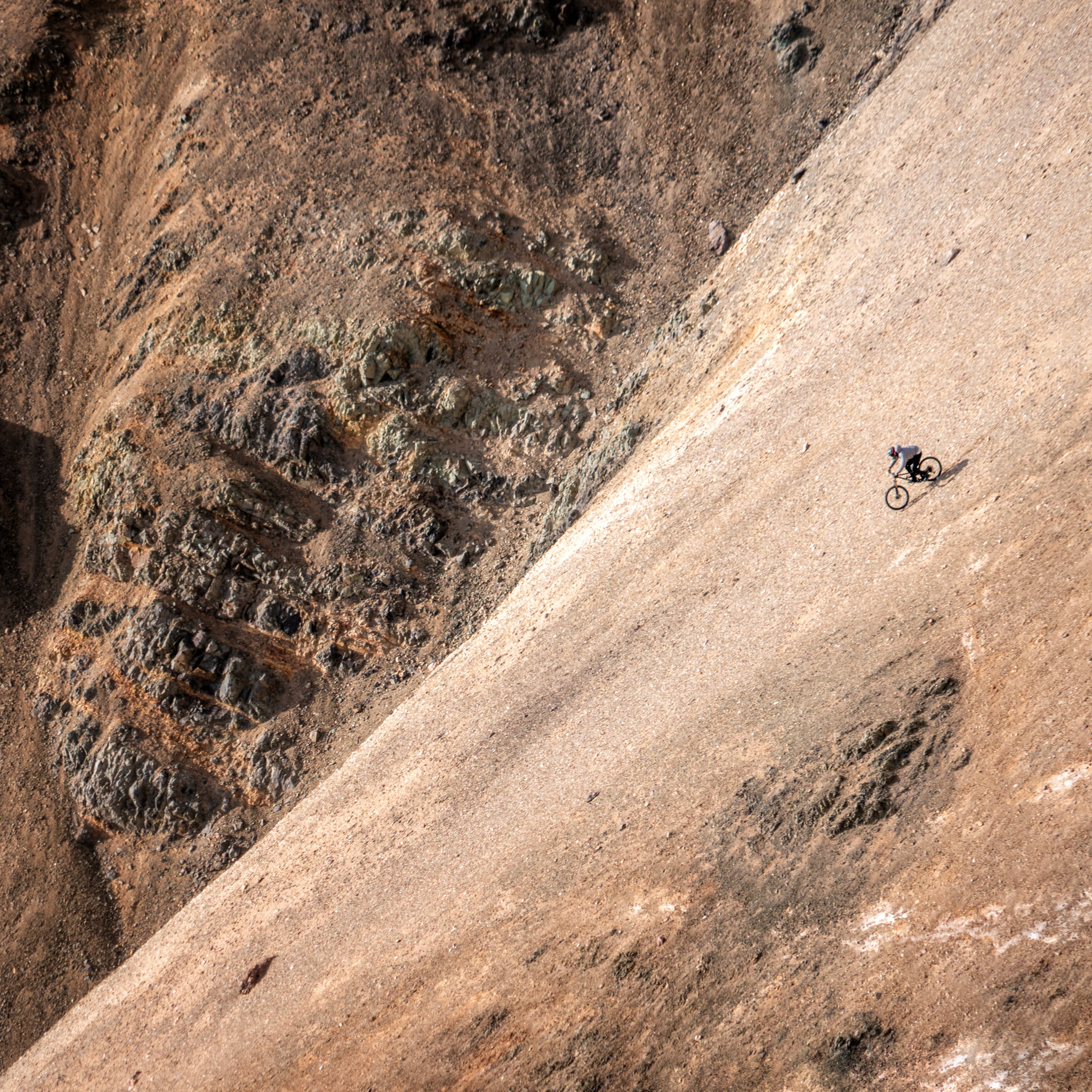 A person is riding a bicycle uphill on a dirt path.  The path is surrounded by rocky hills. 
