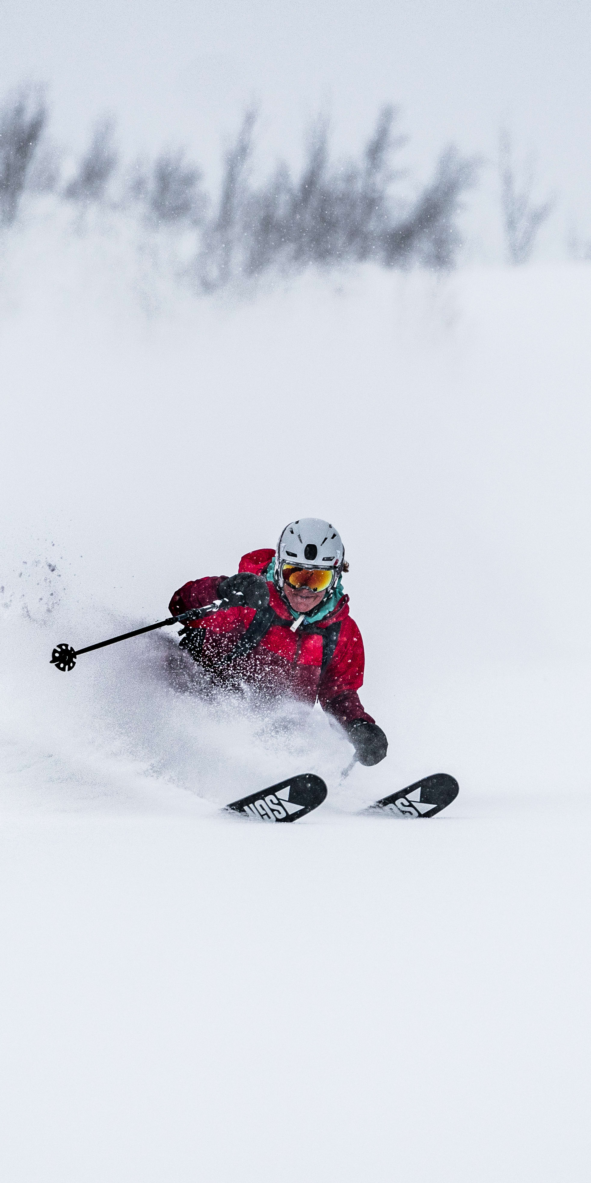A person wearing a red Norrøna jacket skis down a snowy slope.  
