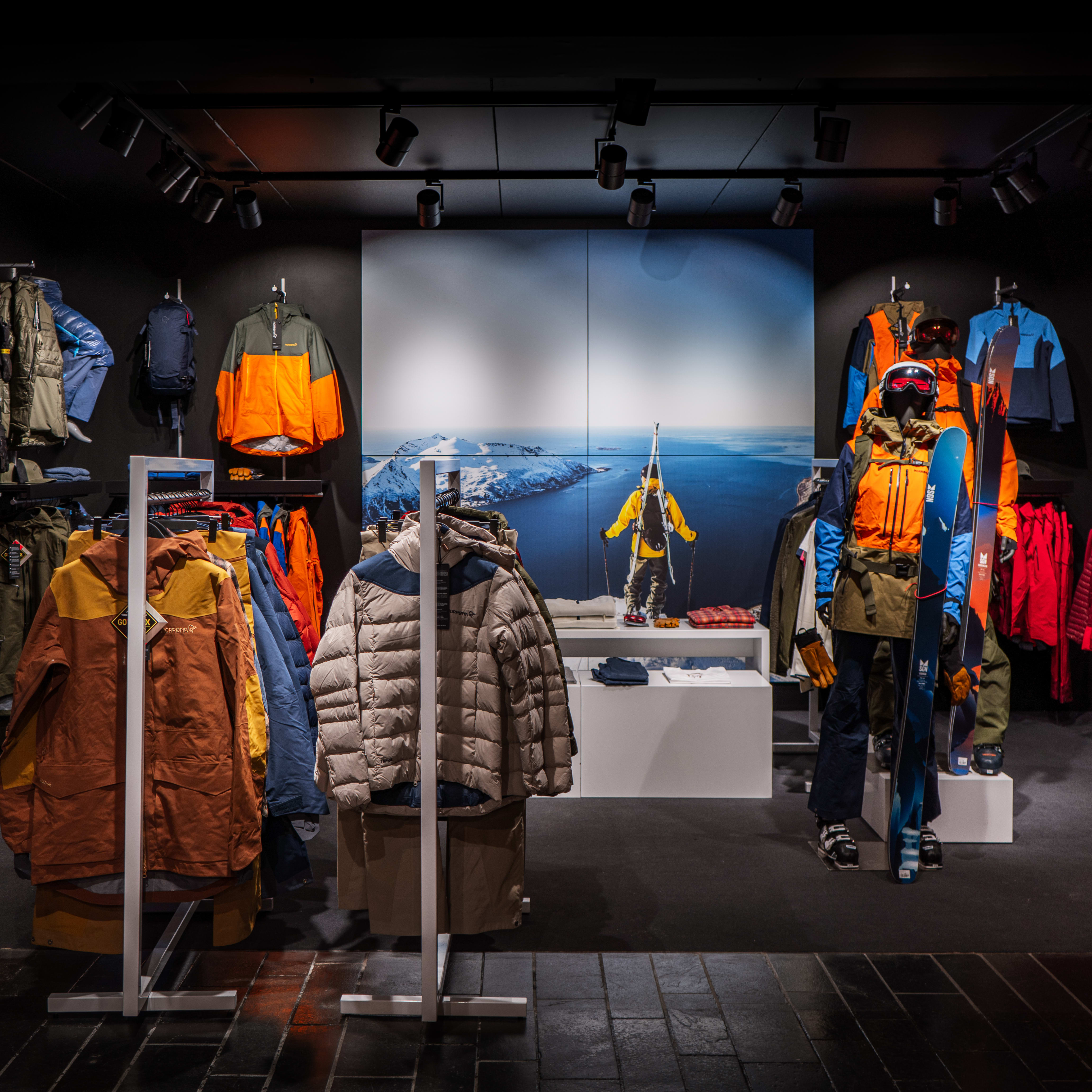A well-lit retail store featuring Norrøna outdoor clothing and gear, with a mannequin wearing a ski jacket and holding skis. 
