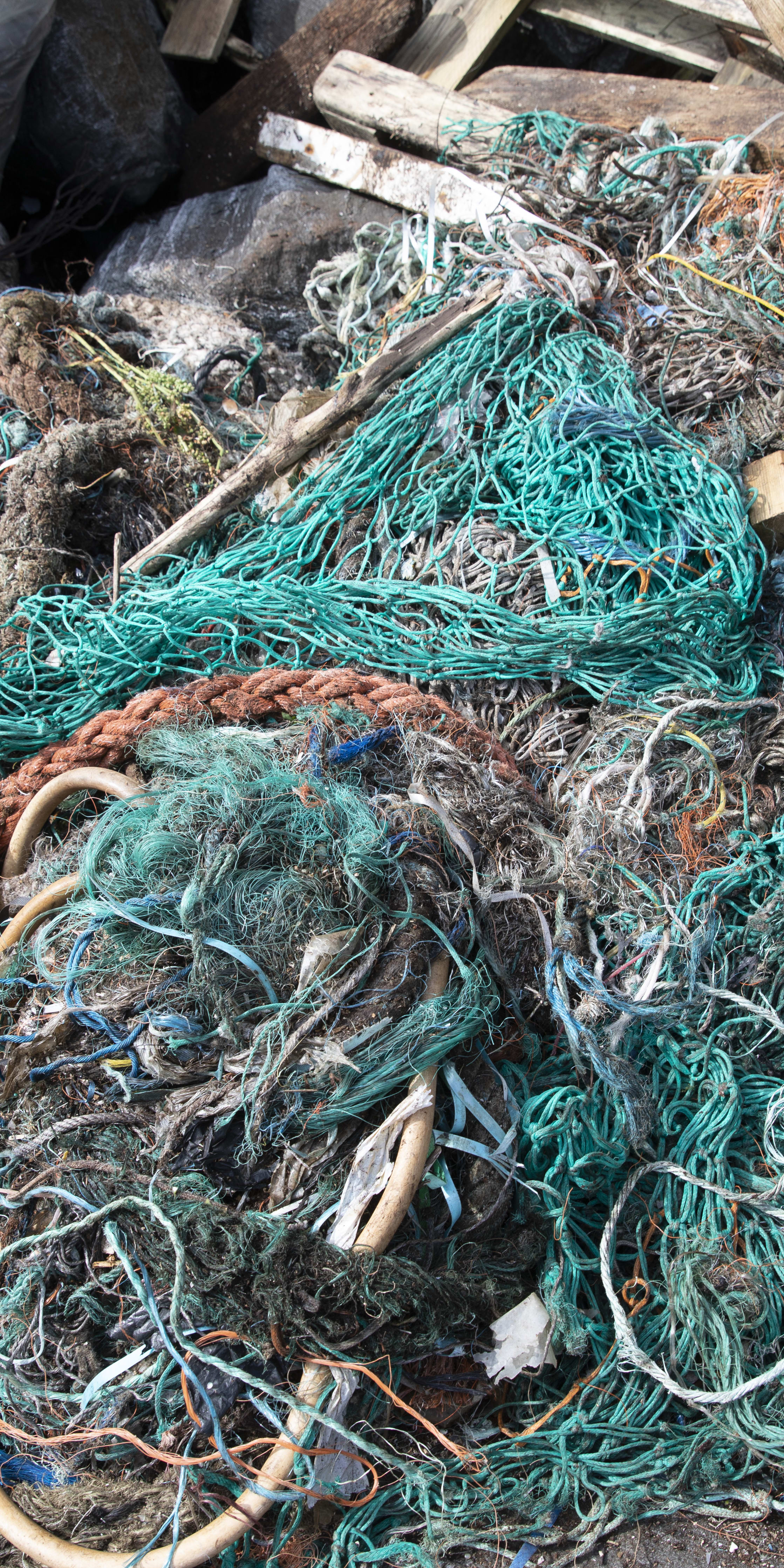 A pile of tangled green, orange, and white ropes and netting with some wood and a plastic bag. 
