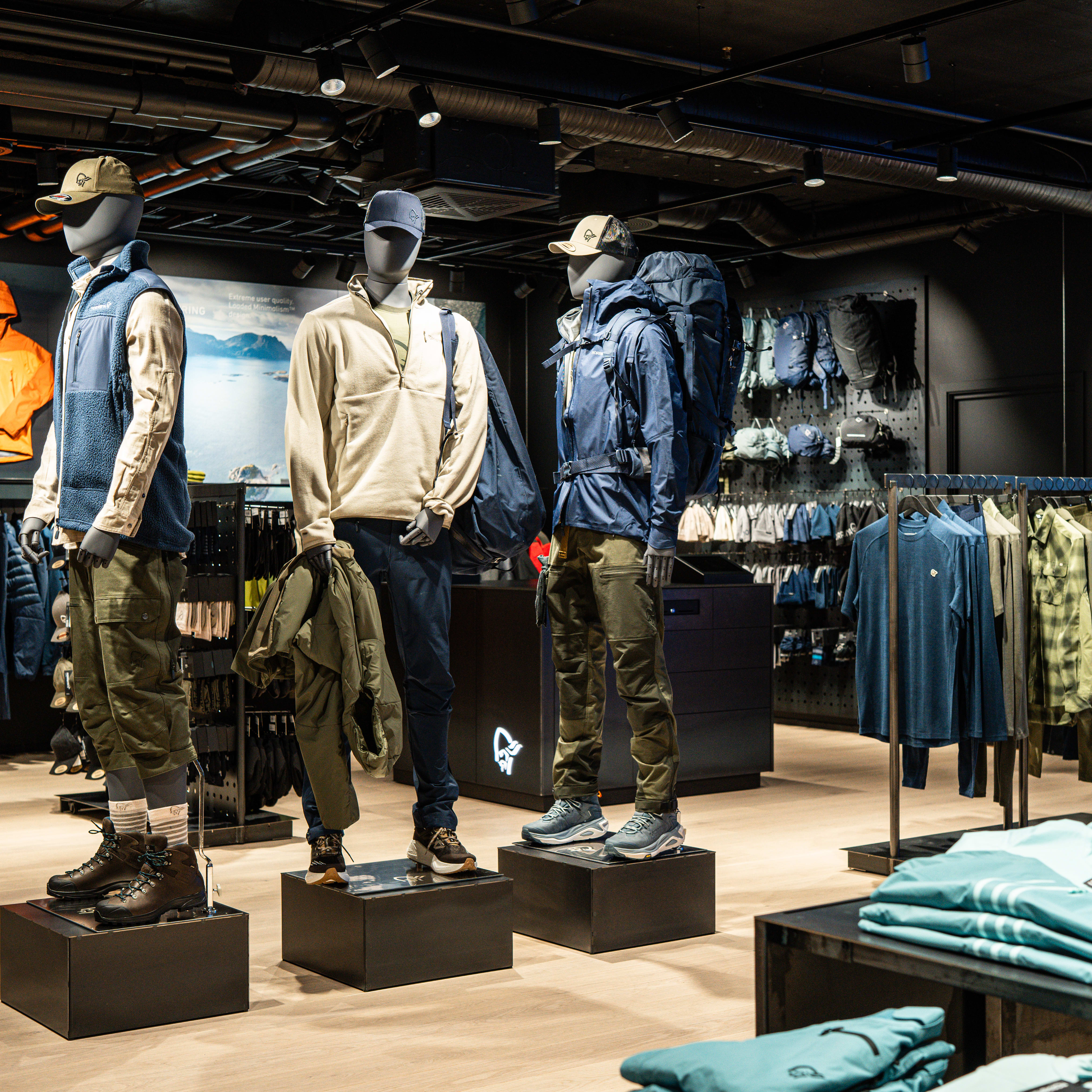 Store display of Norrøna outdoor clothing. Mannequins wear technical apparel and hiking gear. Racks display jackets, shirts, and backpacks.