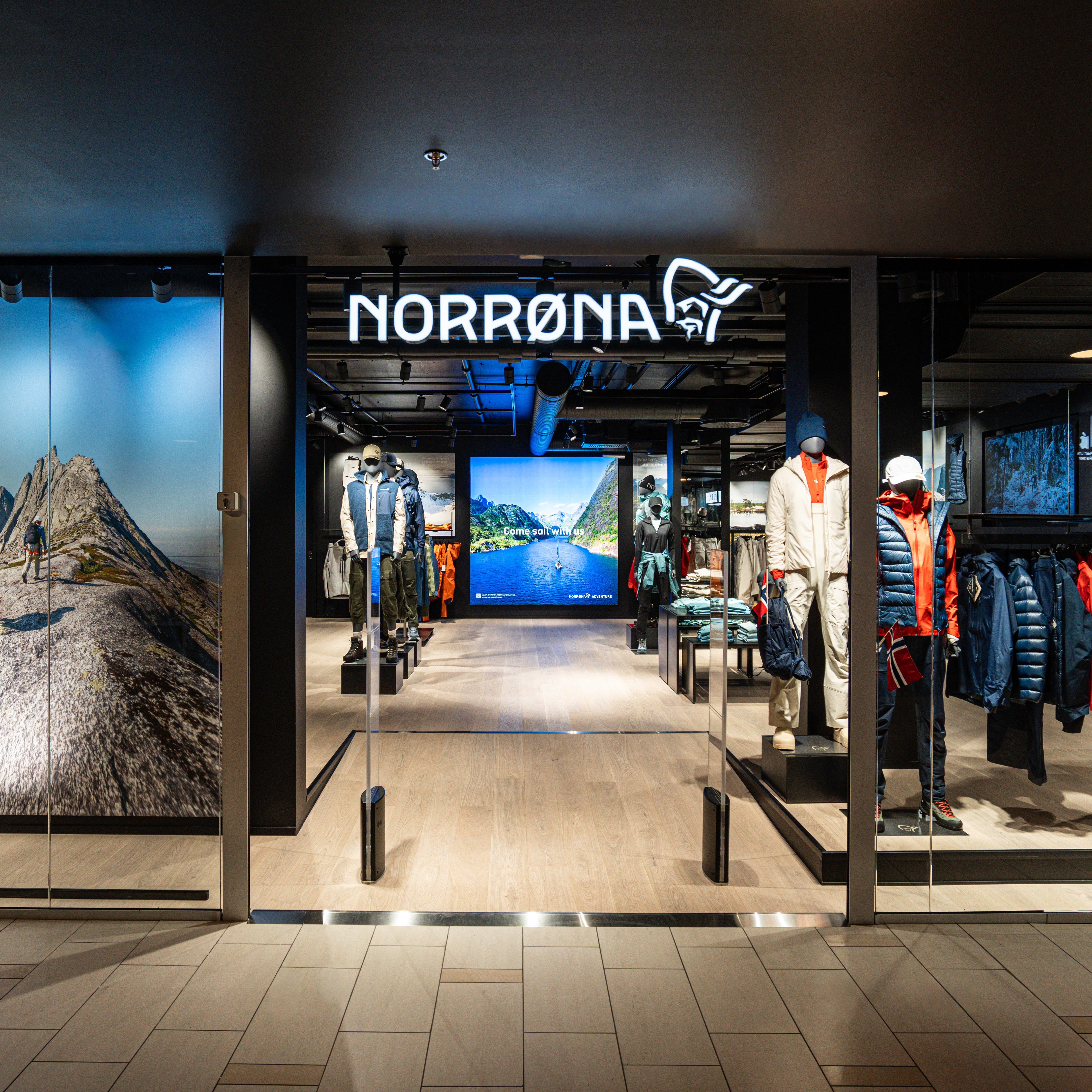 Storefront of Norrøna, a clothing brand. Mannequins wear outdoor apparel. Displays show mountain scenes and clothing racks with Norrøna gear.