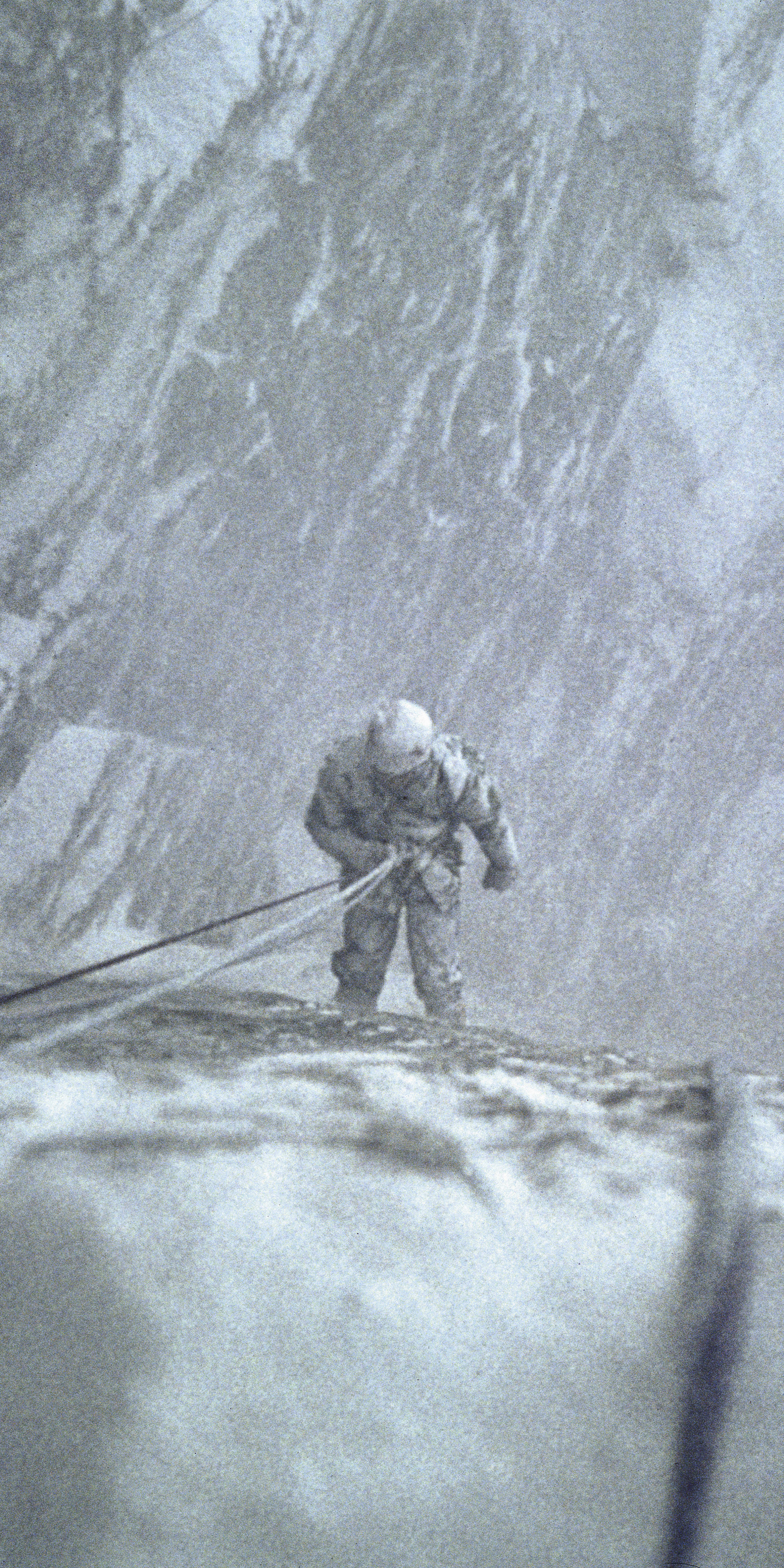 A person rappelling down a snowy mountainside.  The person is wearing a helmet and is attached to a rope.  The mountain is covered in snow and ice.