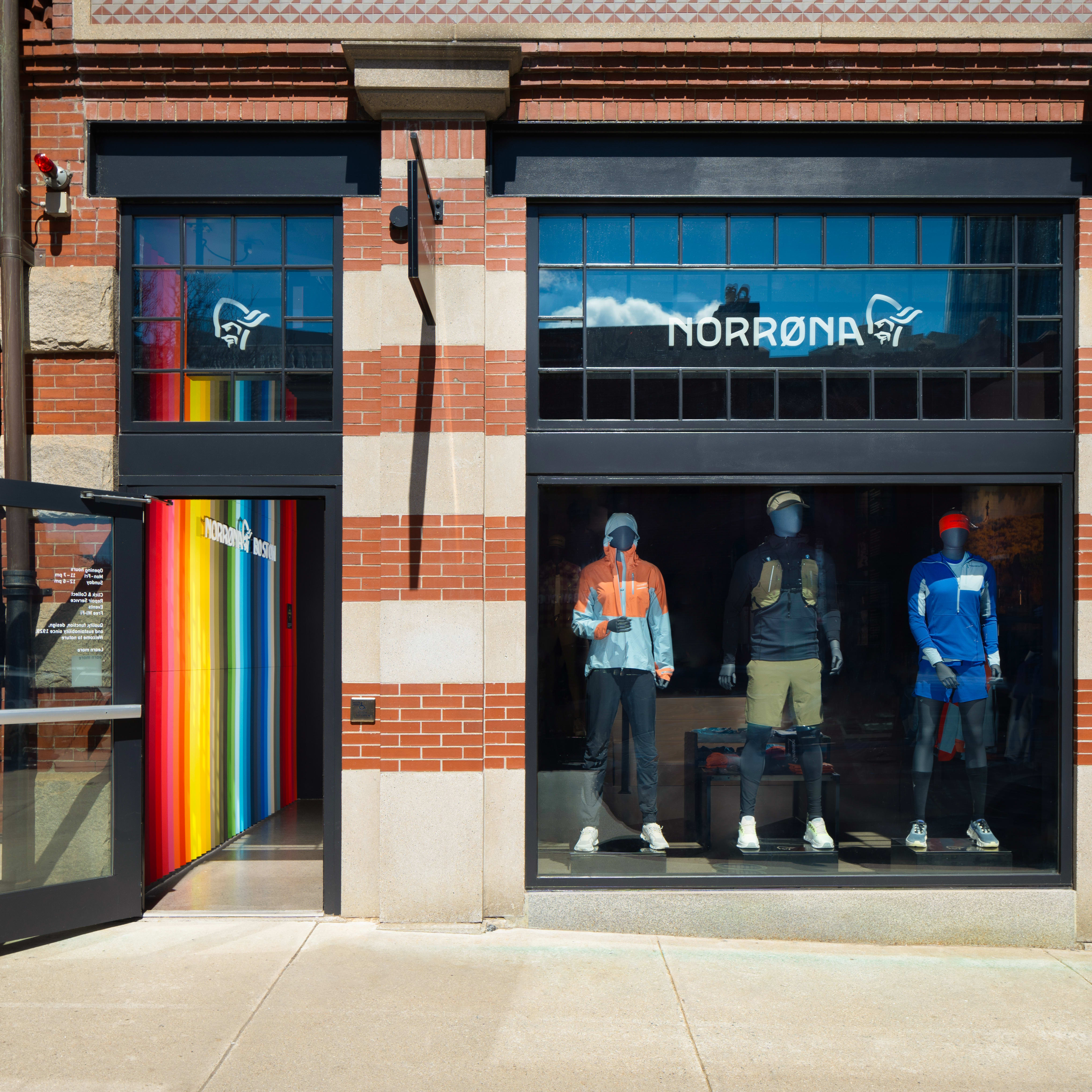 A Norrøna storefront with a rainbow striped door and mannequins displaying clothing in the windows. 
