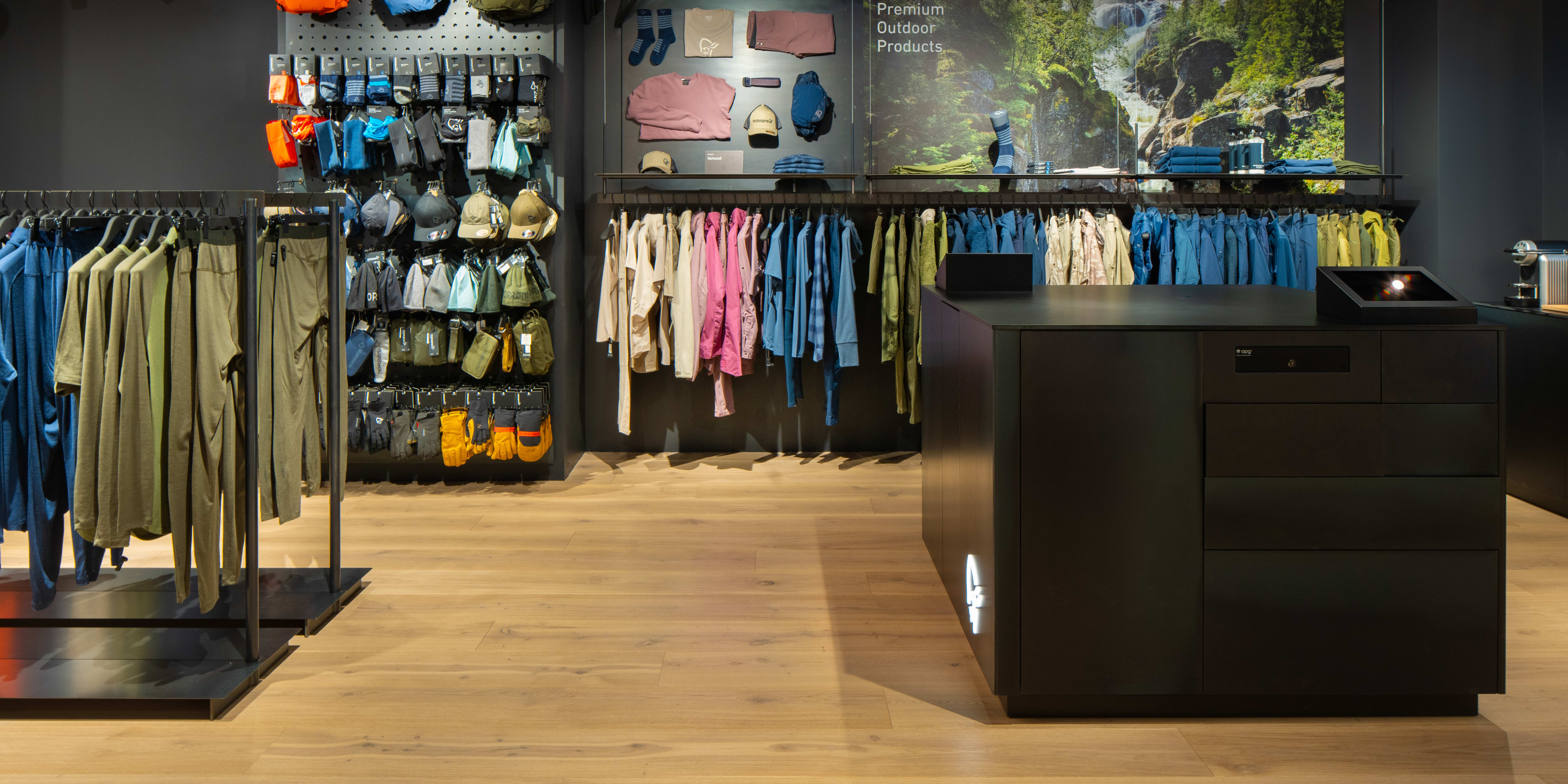 A Norrøna clothing store interior with wooden floors, clothing racks, and a black counter. 
