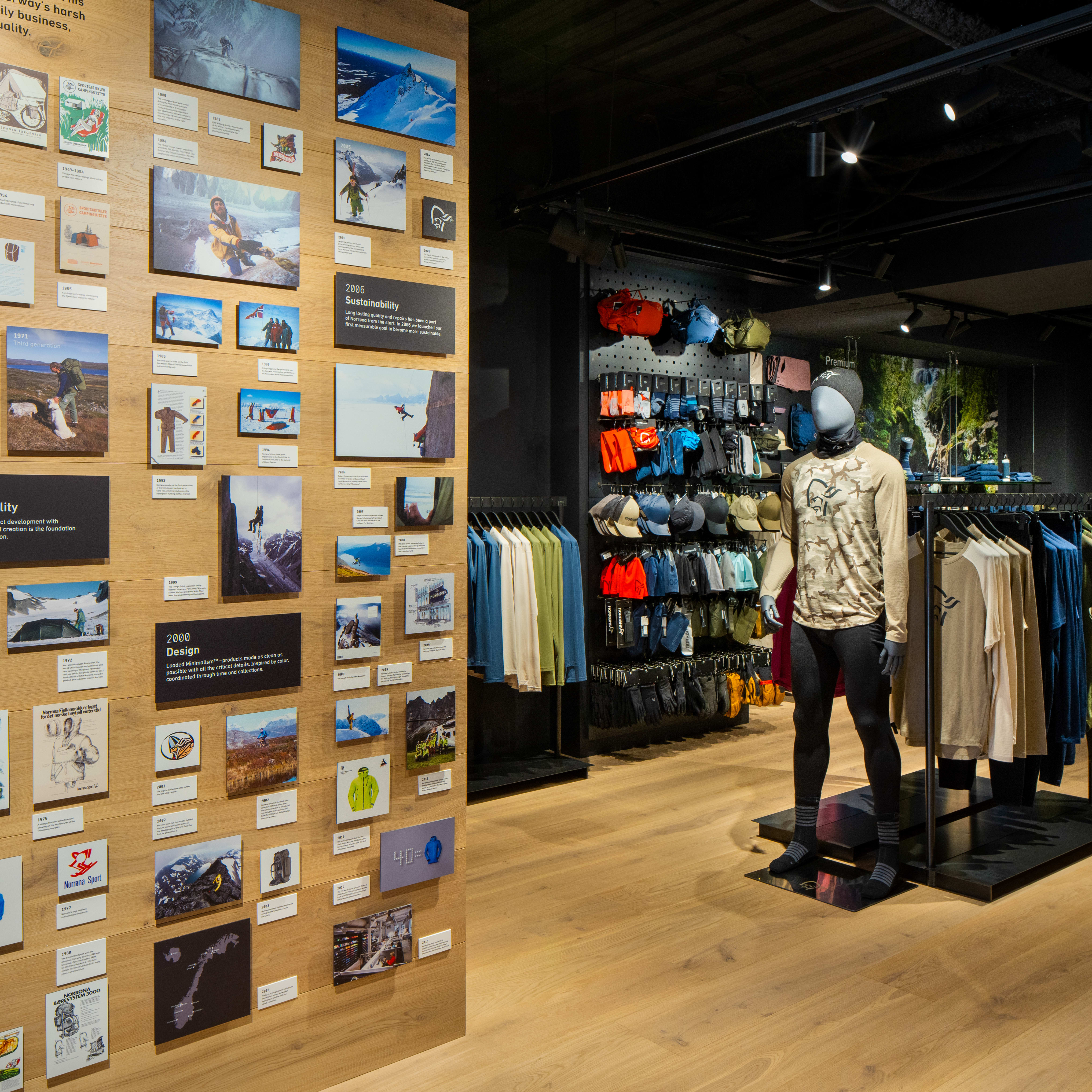 A retail store interior with a wall of framed photos showcasing the history of Norrøna clothing.  A mannequin wears Norrøna clothing in the foreground. 
