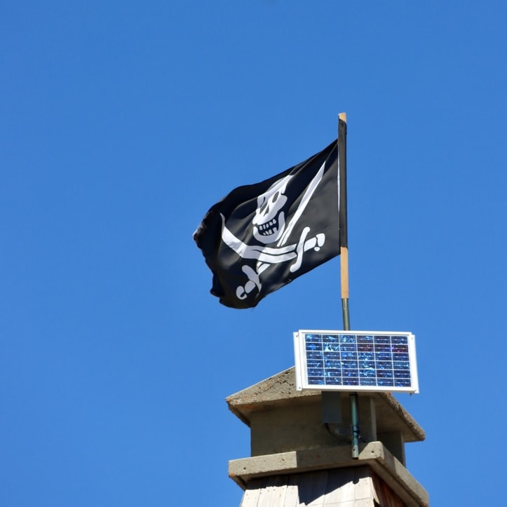 A pirate flag with a white skull and crossbones on a black background is waving atop a chimney. A solar panel is mounted next to the flag.