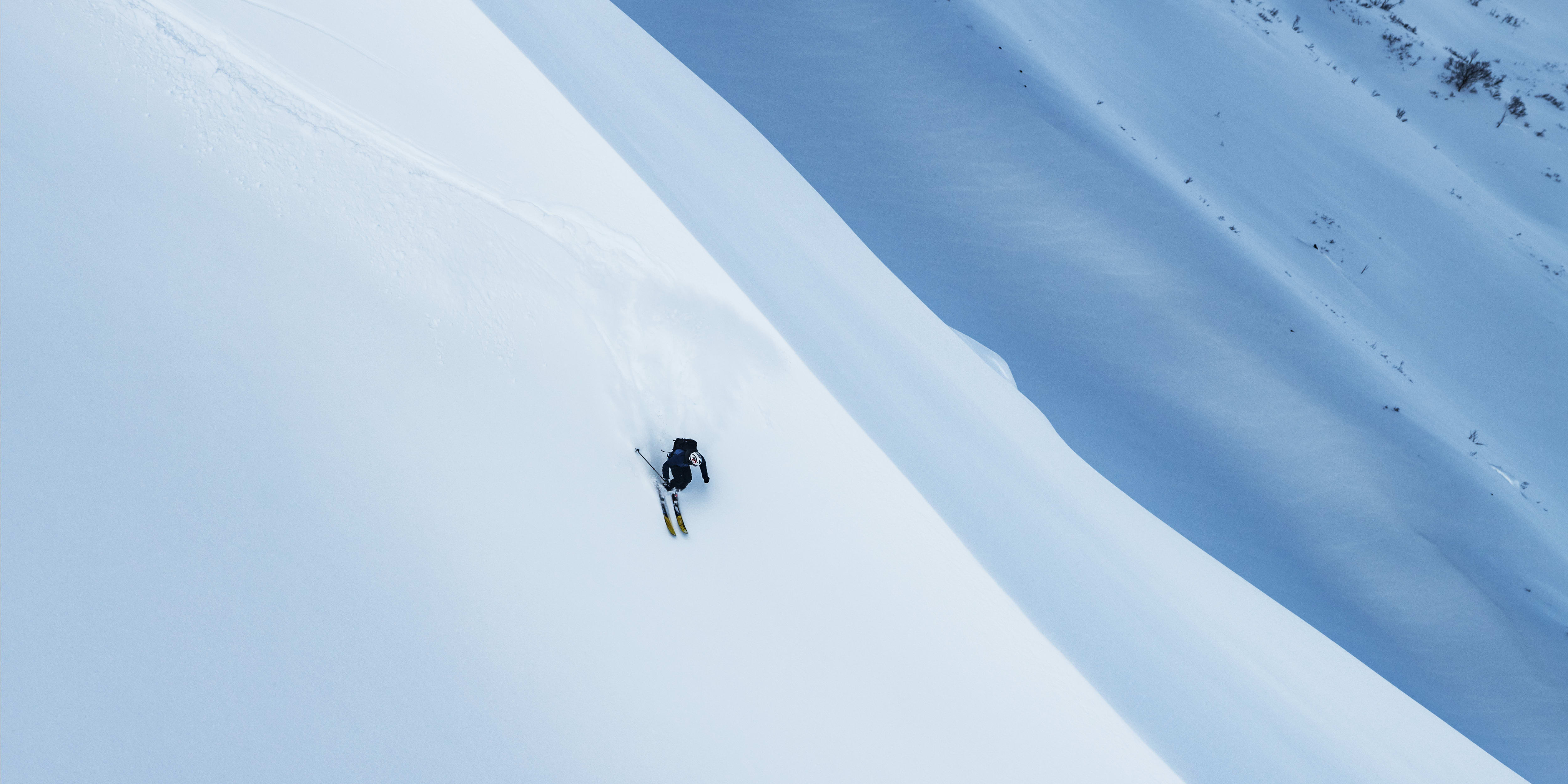Overhead shot of a skier in Norrøna apparel skiing down a steep, snow-covered mountain, leaving tracks in the fresh powder.