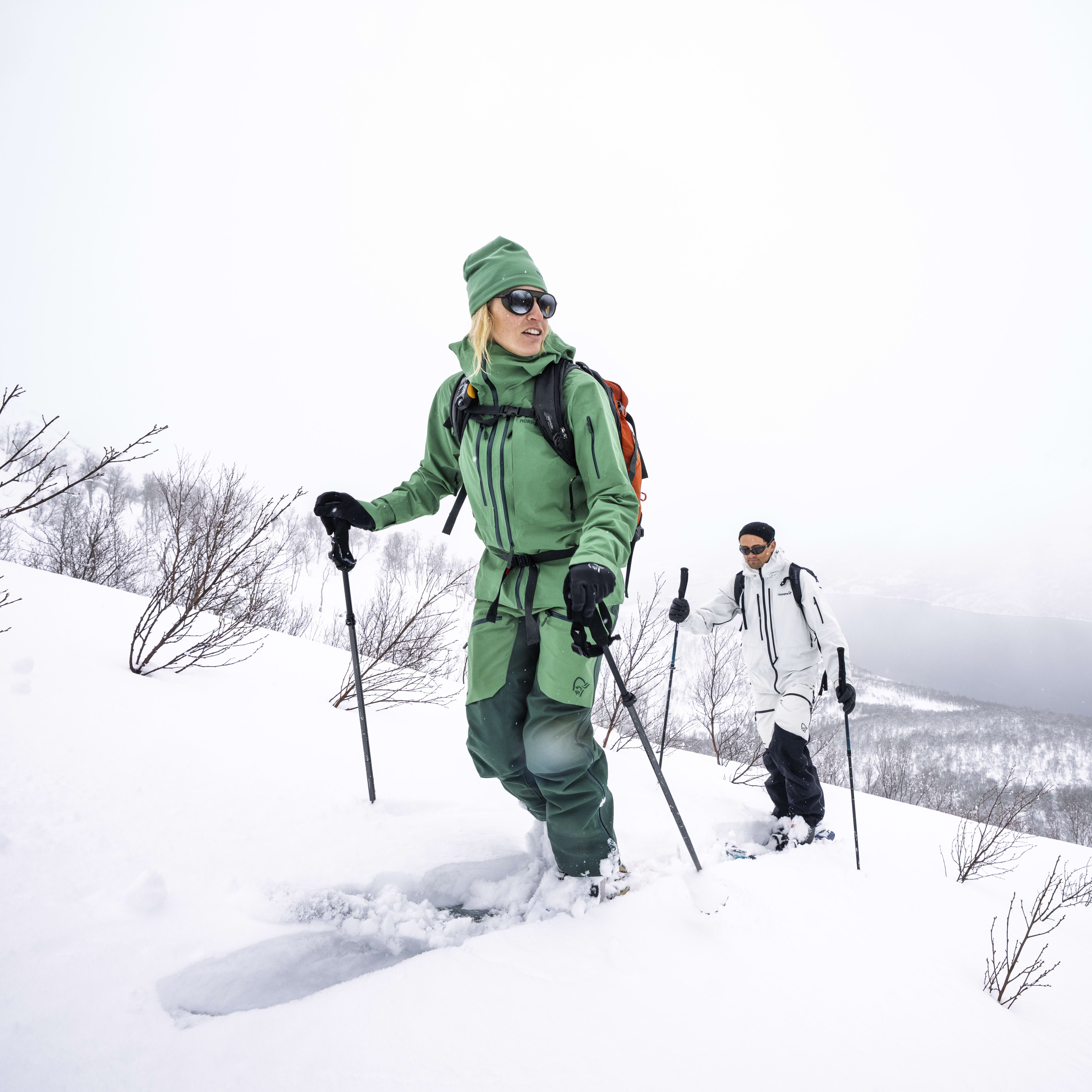 Two people are snowshoeing up a snowy mountainside. The person in the foreground is wearing Norrøna clothing.