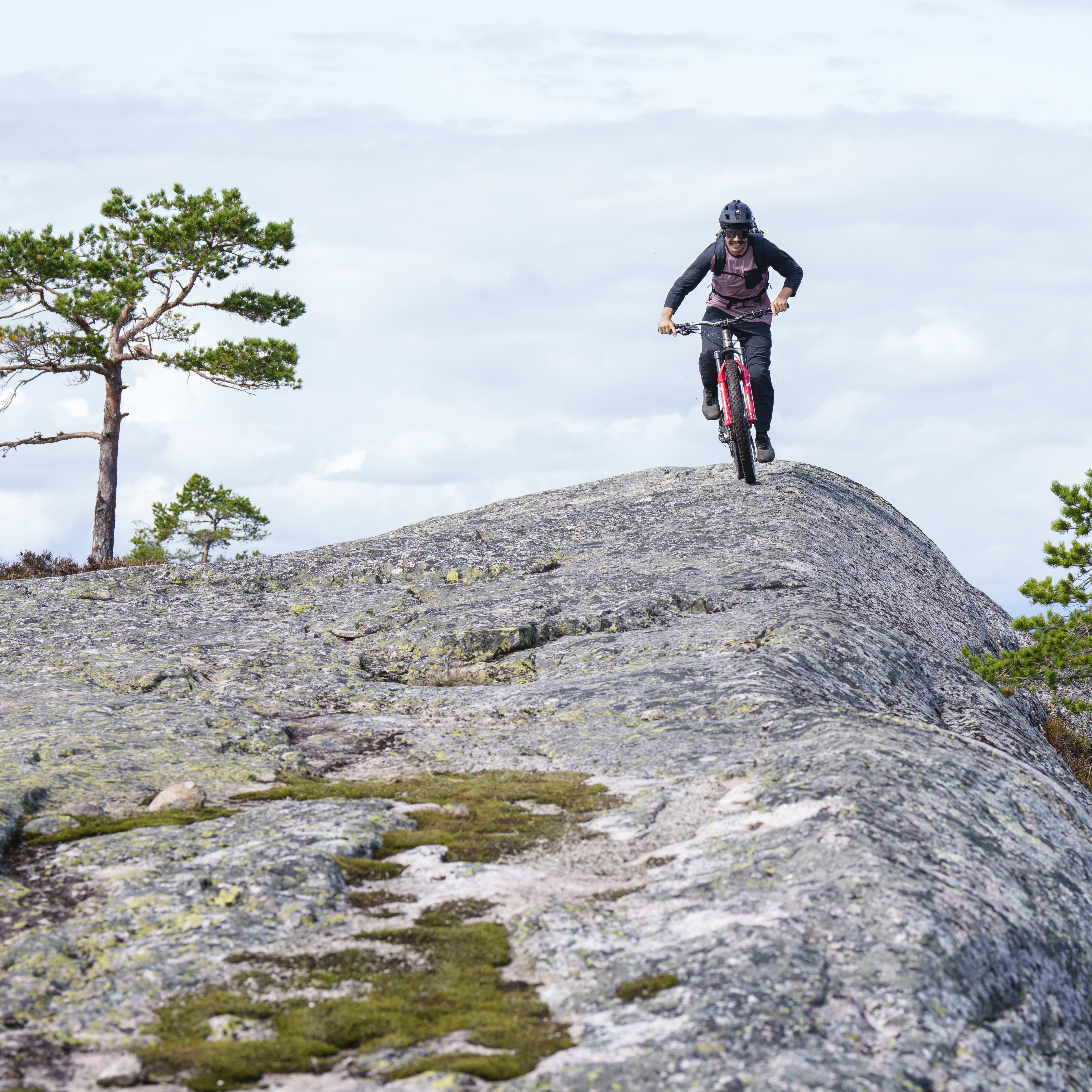 A person wearing a helmet and Norrøna clothing rides a bicycle down a rocky slope.