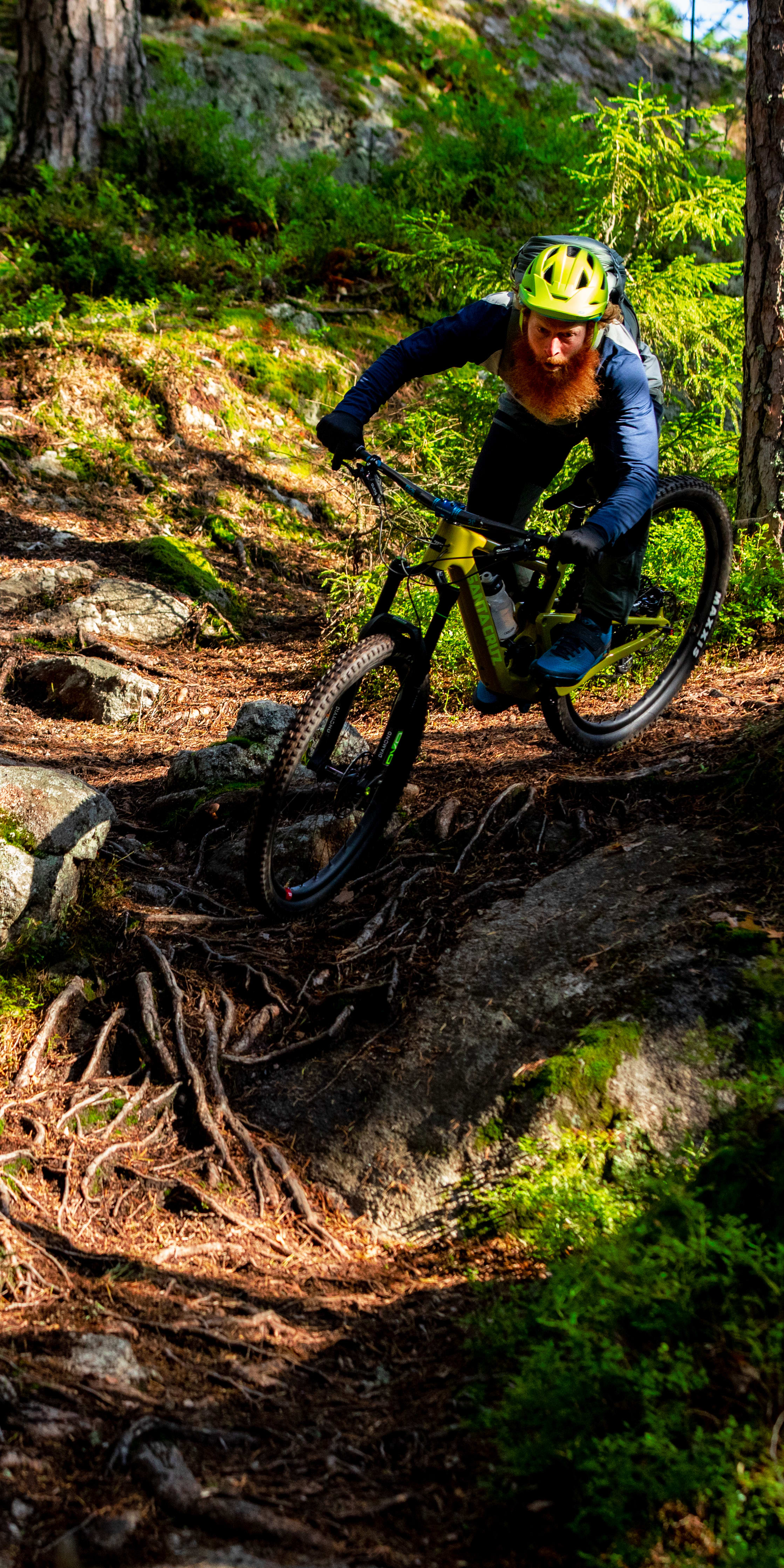 A person wearing a Norrøna cycling outfit rides a mountain bike on a rocky trail through a forest.