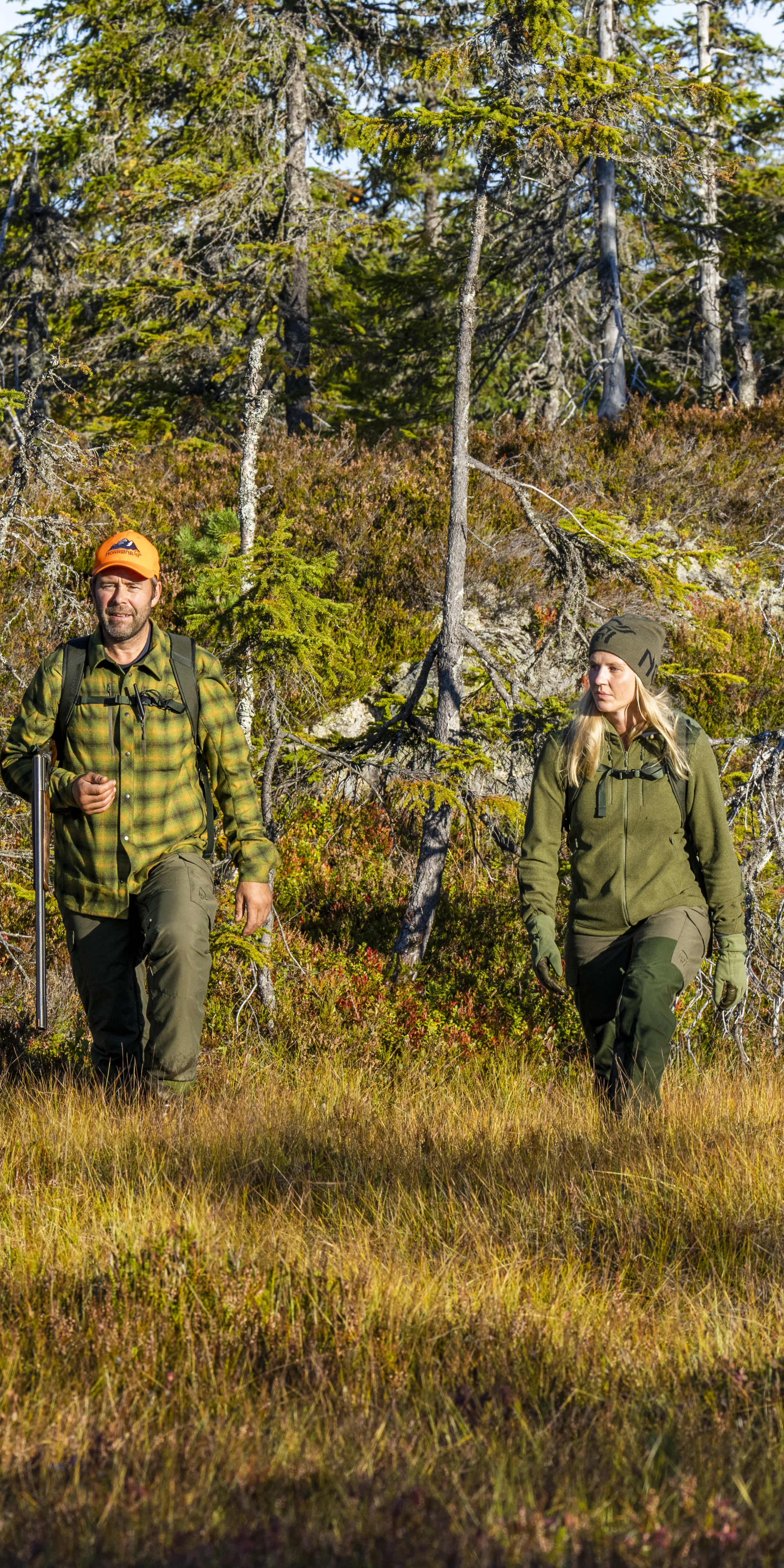 Two people wearing Norrøna clothing walk through a forest clearing. 

