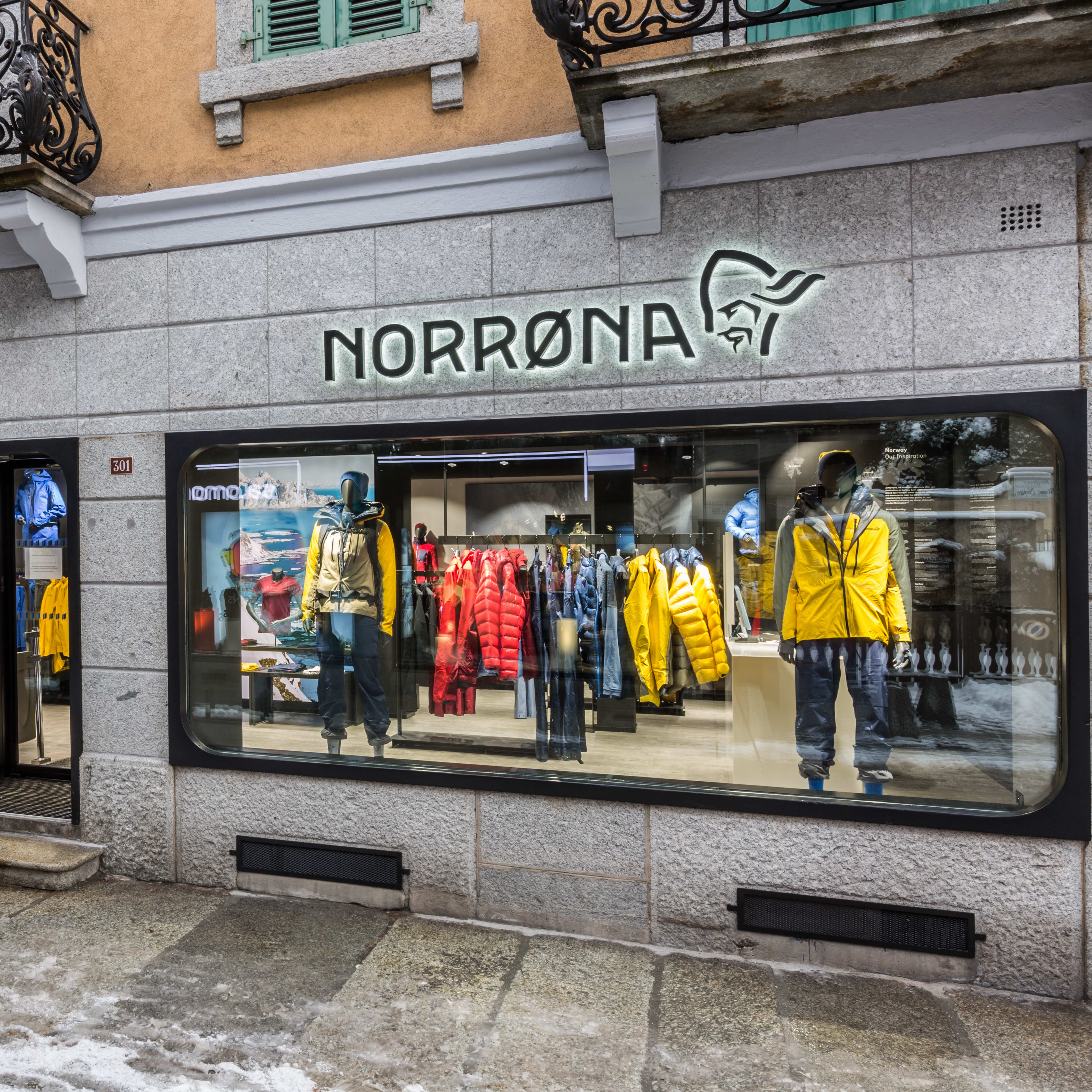 A Norrøna storefront with a window display featuring mannequins wearing outdoor clothing.  The shop is located on a street with snow on the ground. 
