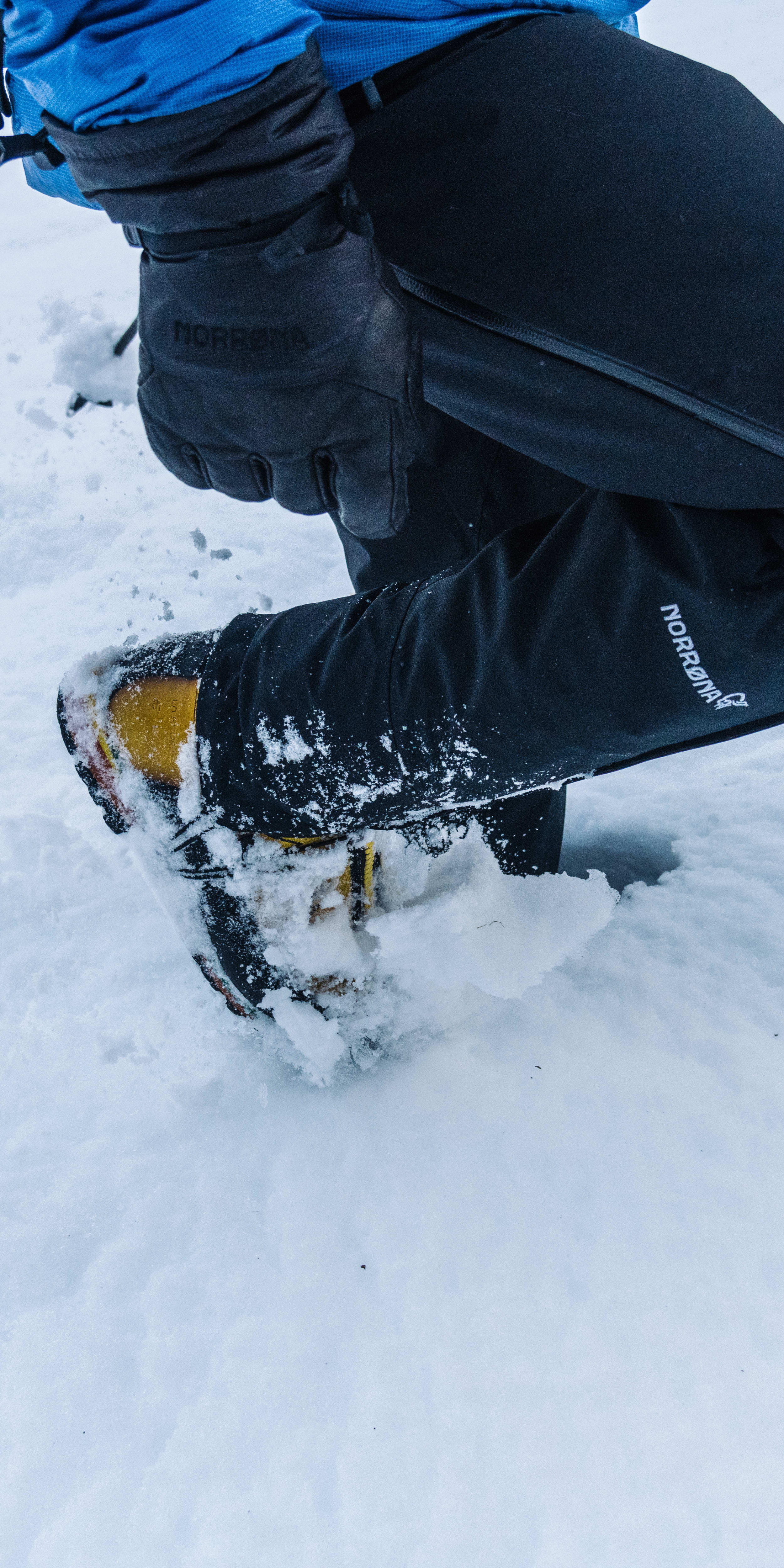 A person's leg wearing Norrøna pants and boots is standing in snow. 
