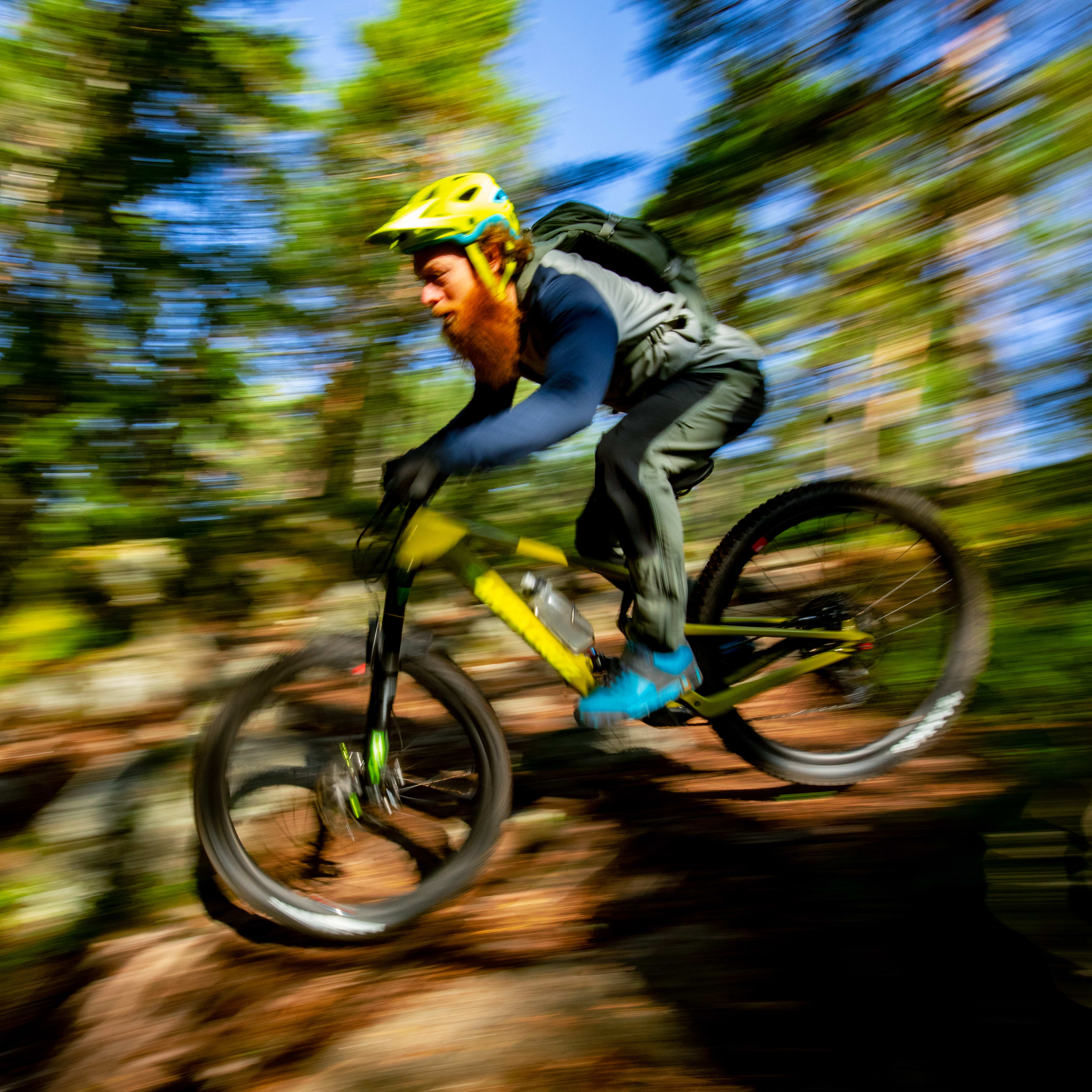 A blurry image of a person riding a mountain bike through a forest. The rider is wearing a helmet and Norrøna clothing.