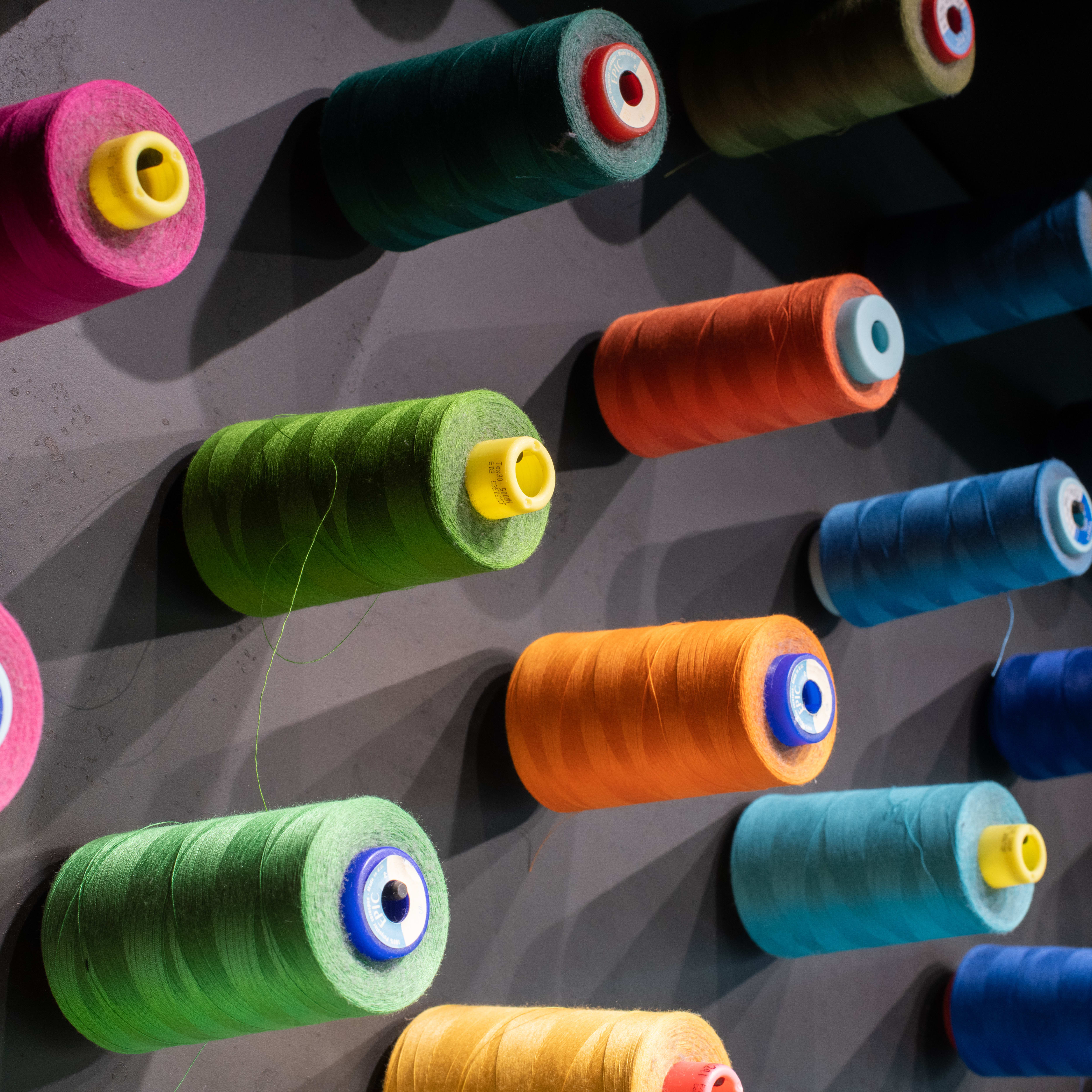 Various spools of colorful thread are displayed on a wall.