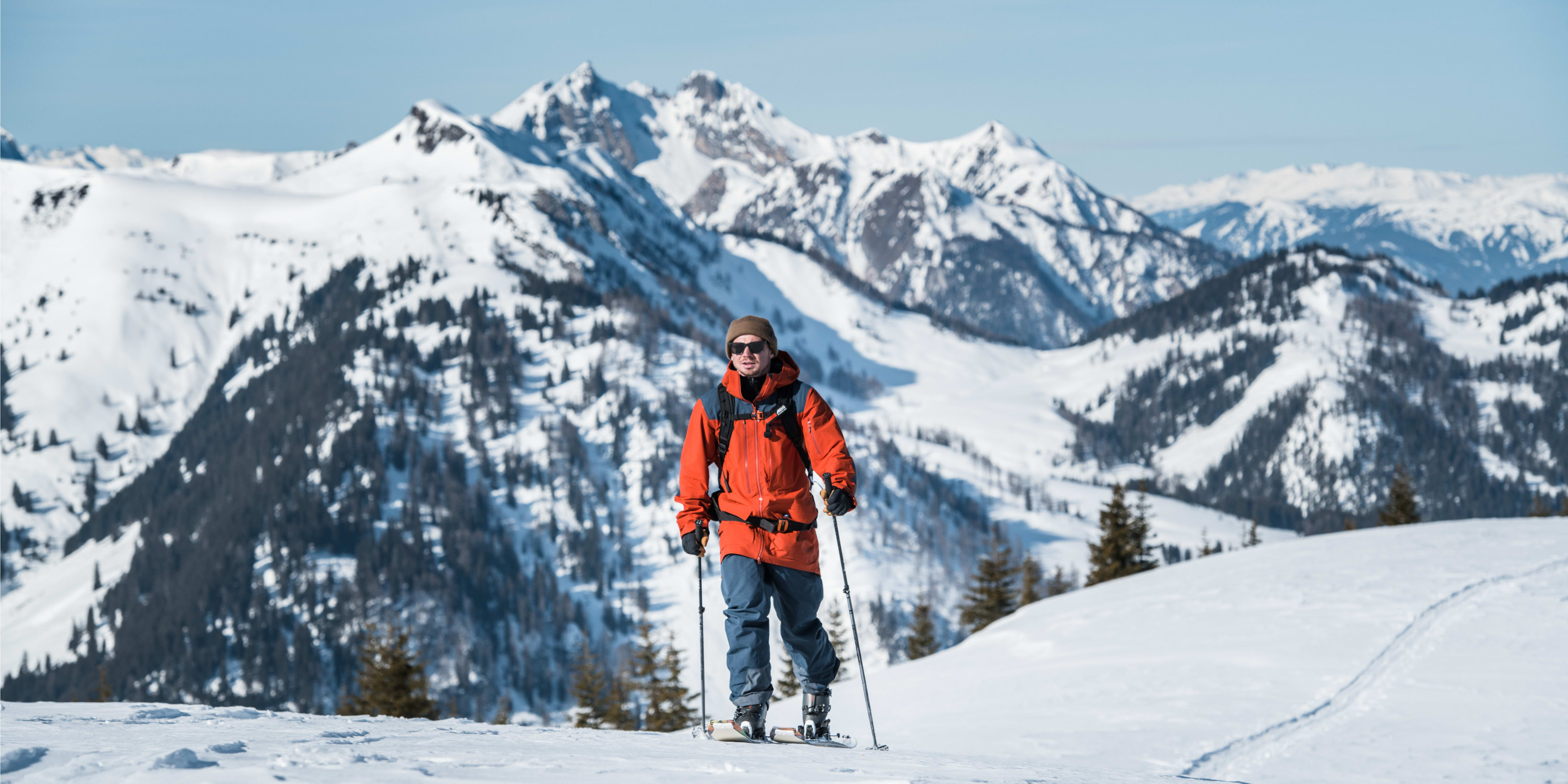 A person wearing Norrøna gear walks on snowshoes across a snow-covered mountaintop. 
