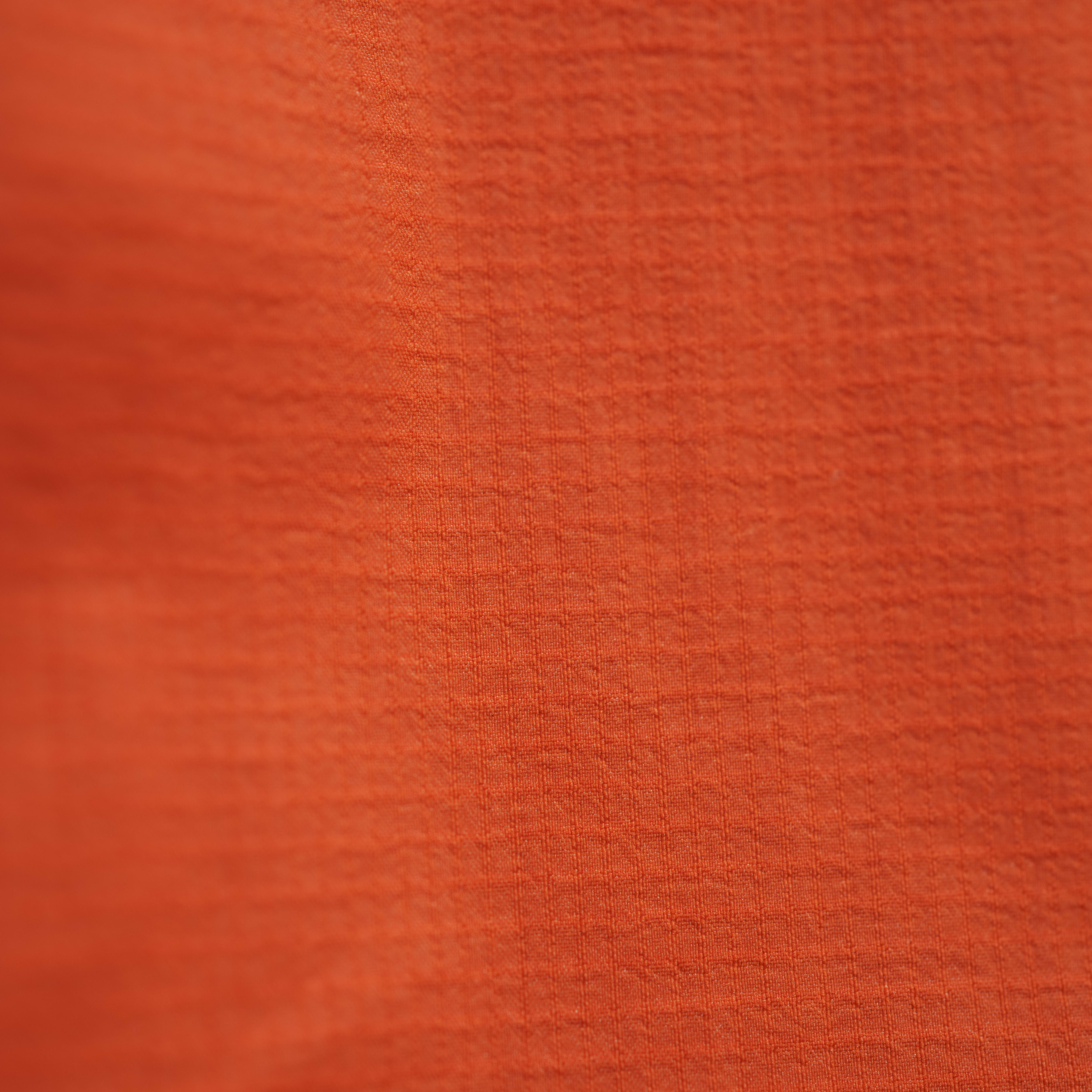Close up of a Norrøna orange jacket, showing the textured fabric. 
