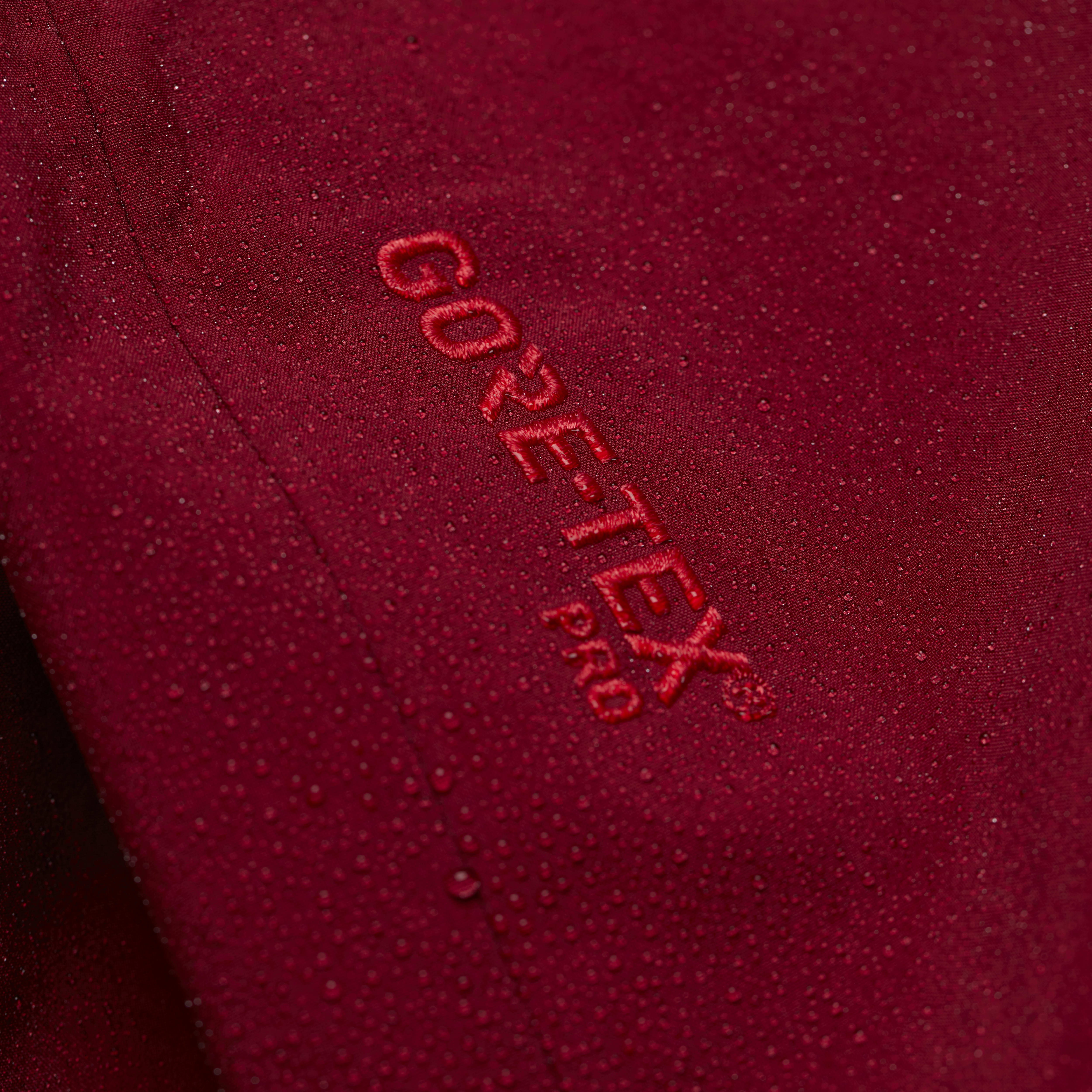 Close-up of a red Norrøna jacket with water droplets. The "GORE-TEX Pro" logo is visible.