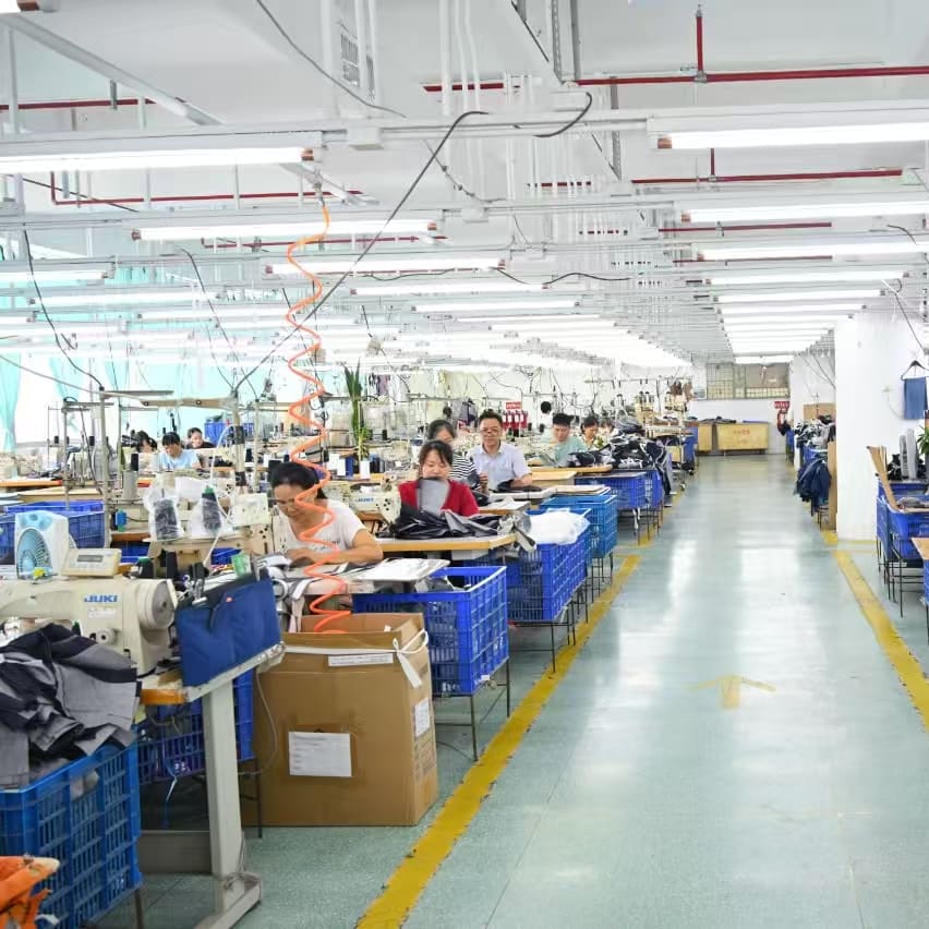 A brightly lit clothing factory with rows of workers at sewing machines, producing Norrøna apparel. Blue bins are present throughout the production line.
