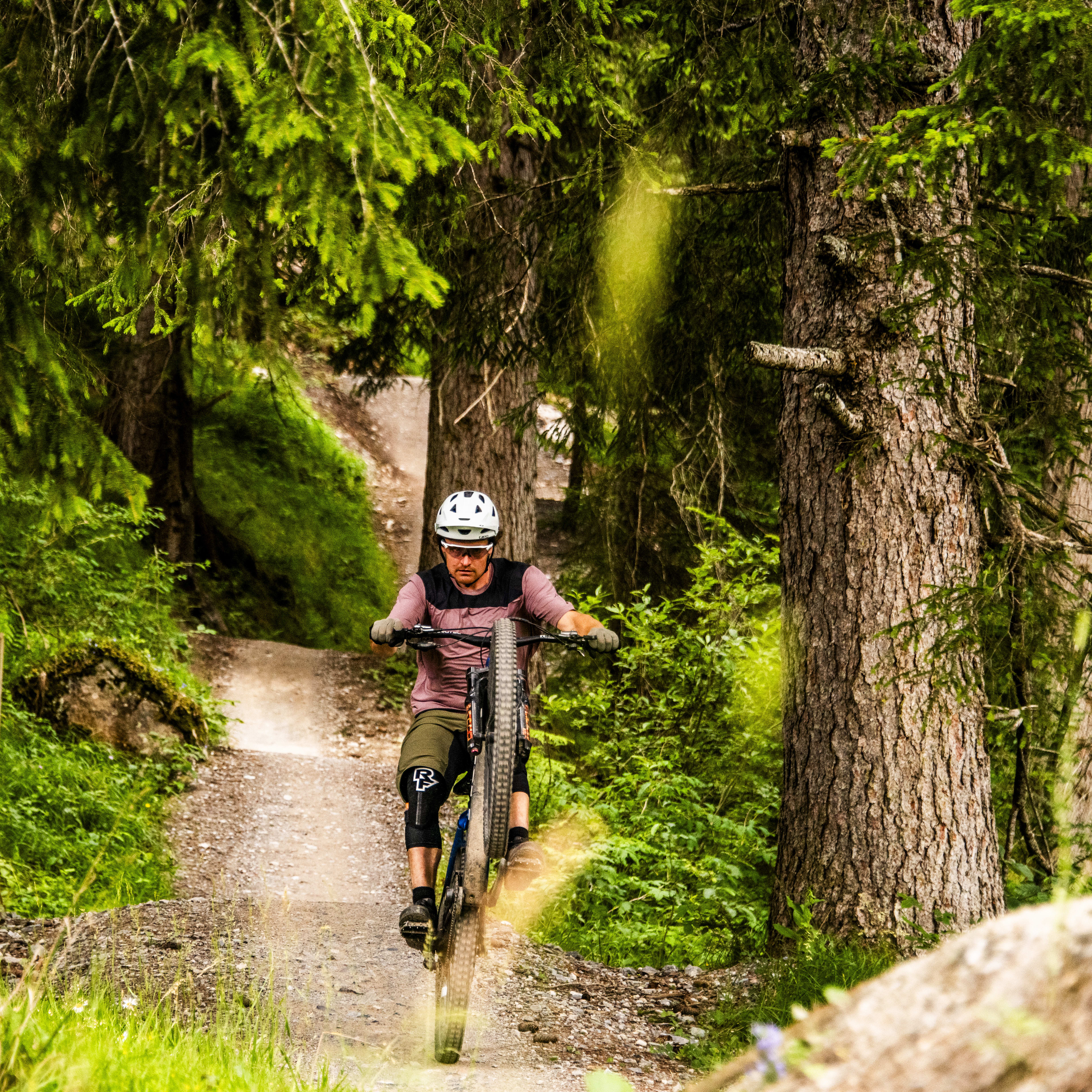 A man wearing a helmet and Norrøna clothing rides a mountain bike on a dirt path through a forest.