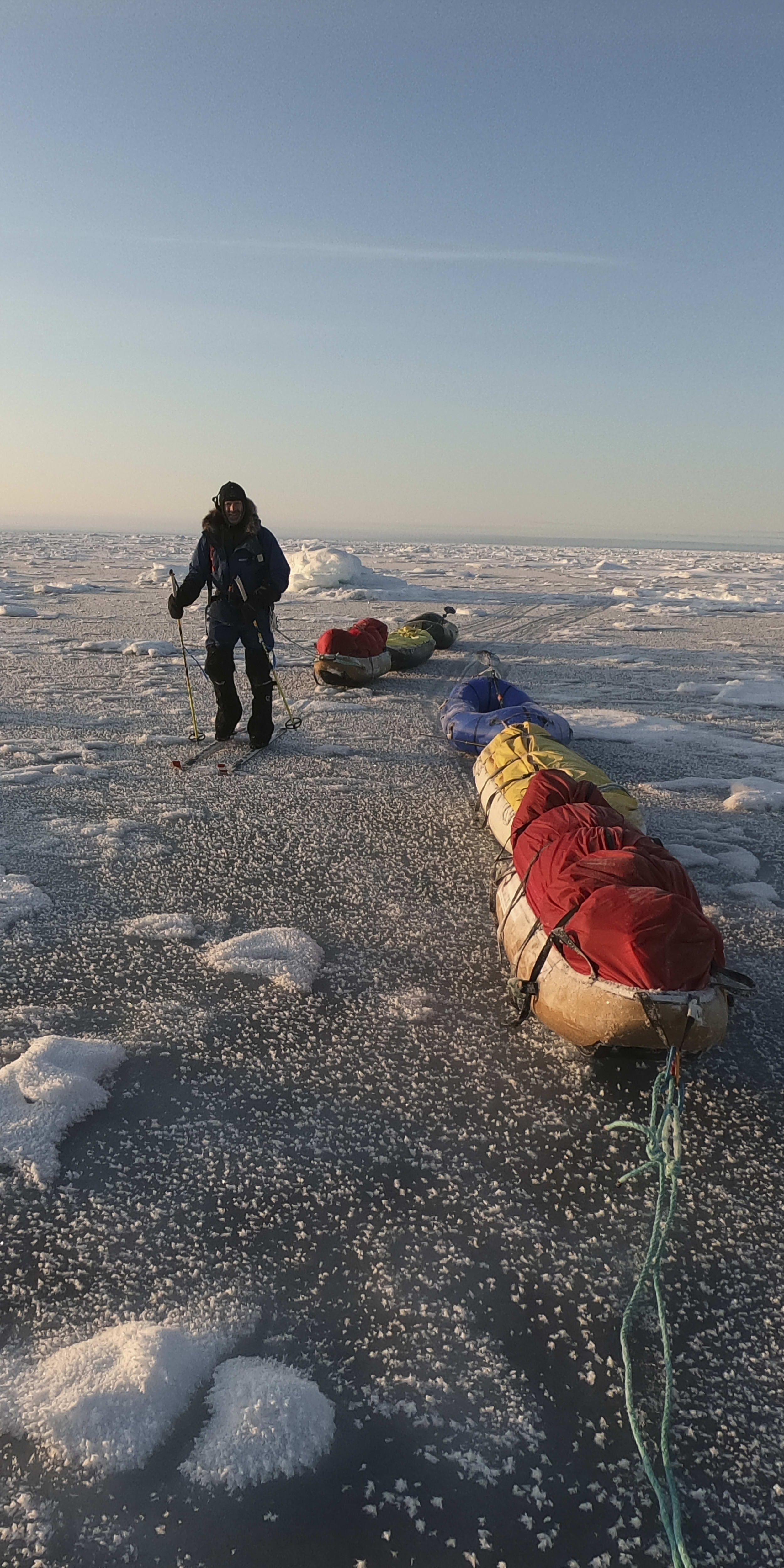 A person cross-country skiing on a frozen lake, pulling behind them a sled loaded with supplies.