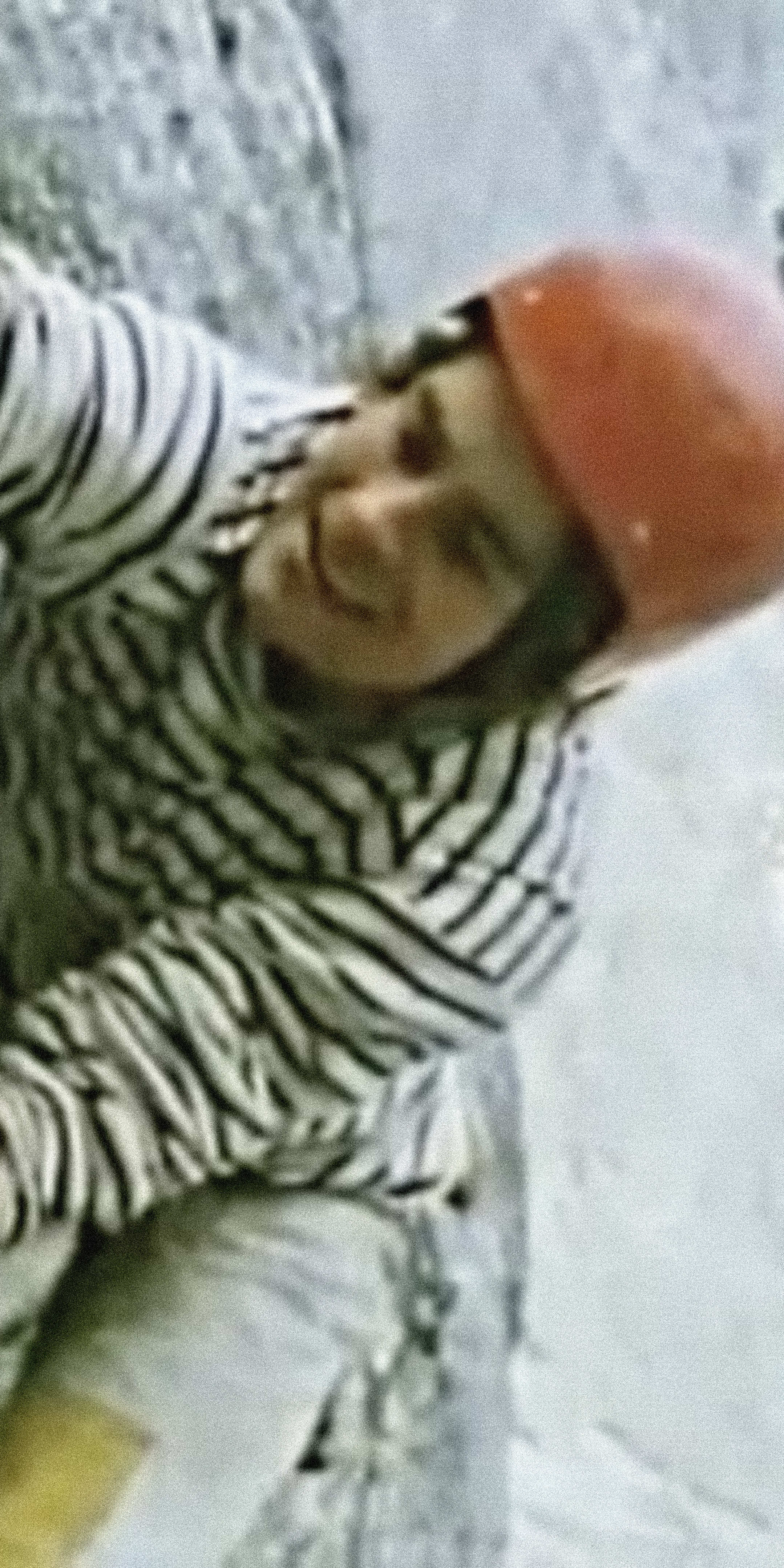 A person wearing a red helmet and striped shirt is climbing a rock face. Their hands are gripping the rock, and they are looking down.