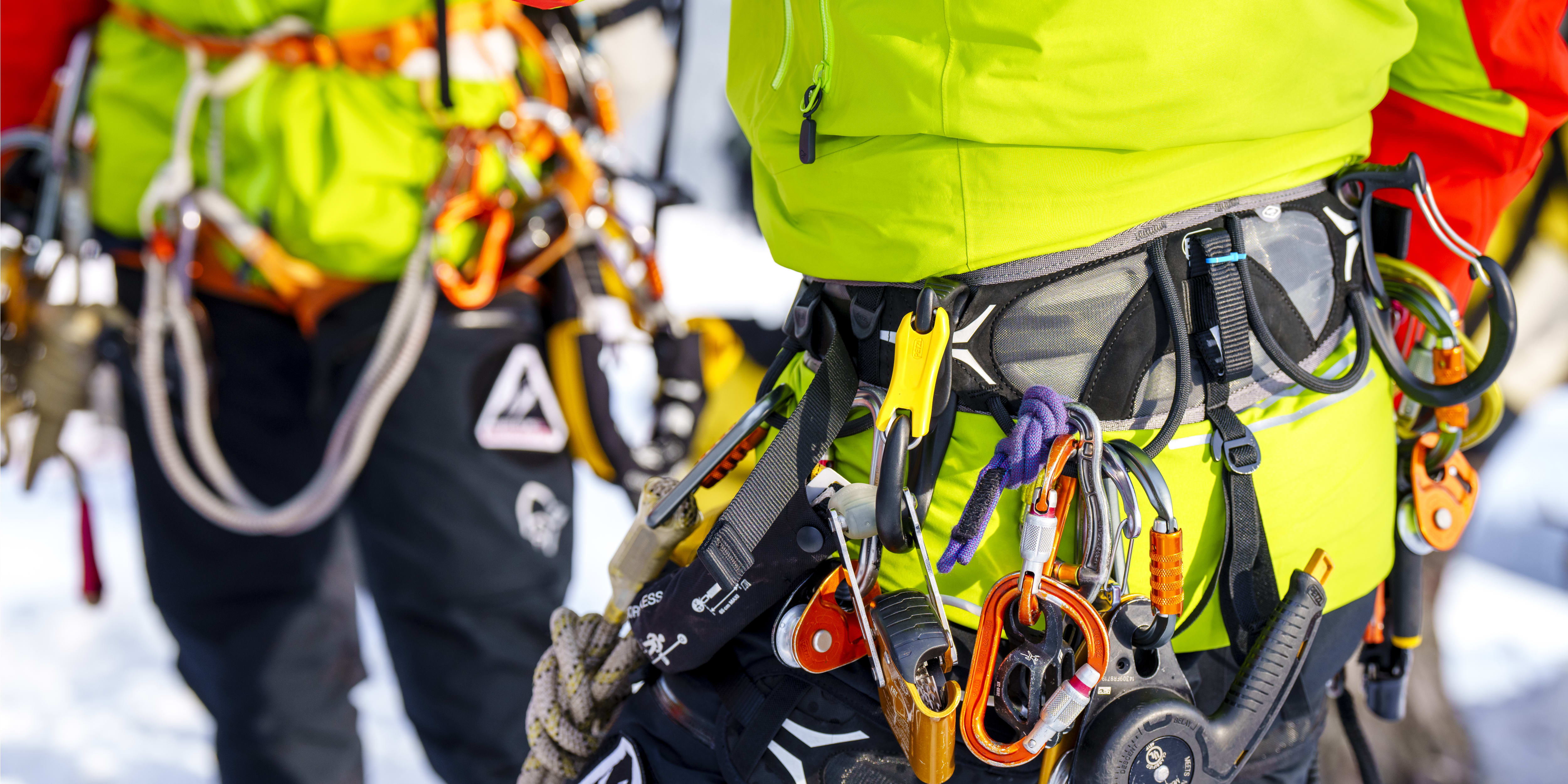 Close-up of a climber wearing a Norrøna jacket and harness, with a variety of climbing gear attached. 
