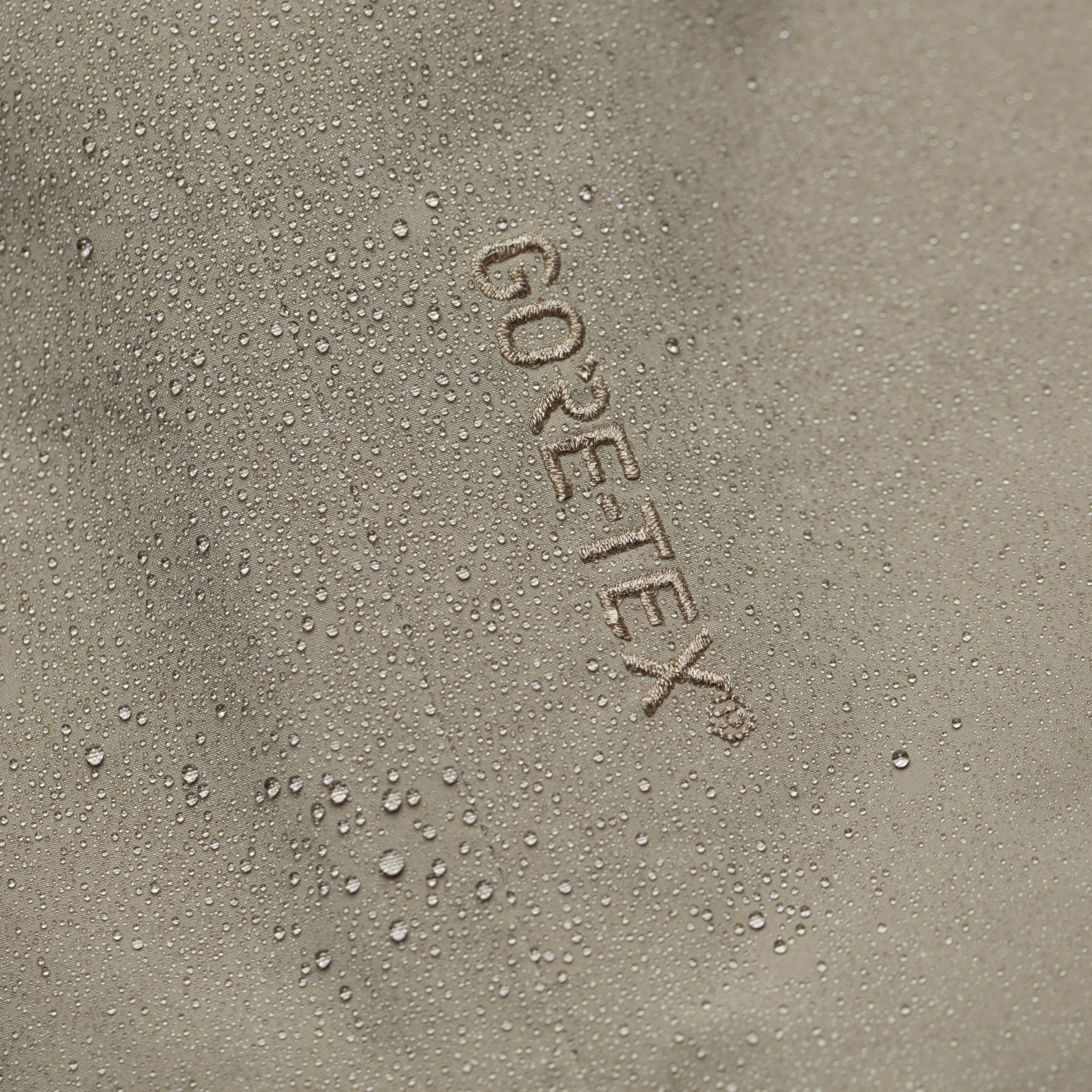 Water droplets on a beige Norrøna garment with "GORE-TEX" embroidered on the fabric. 
