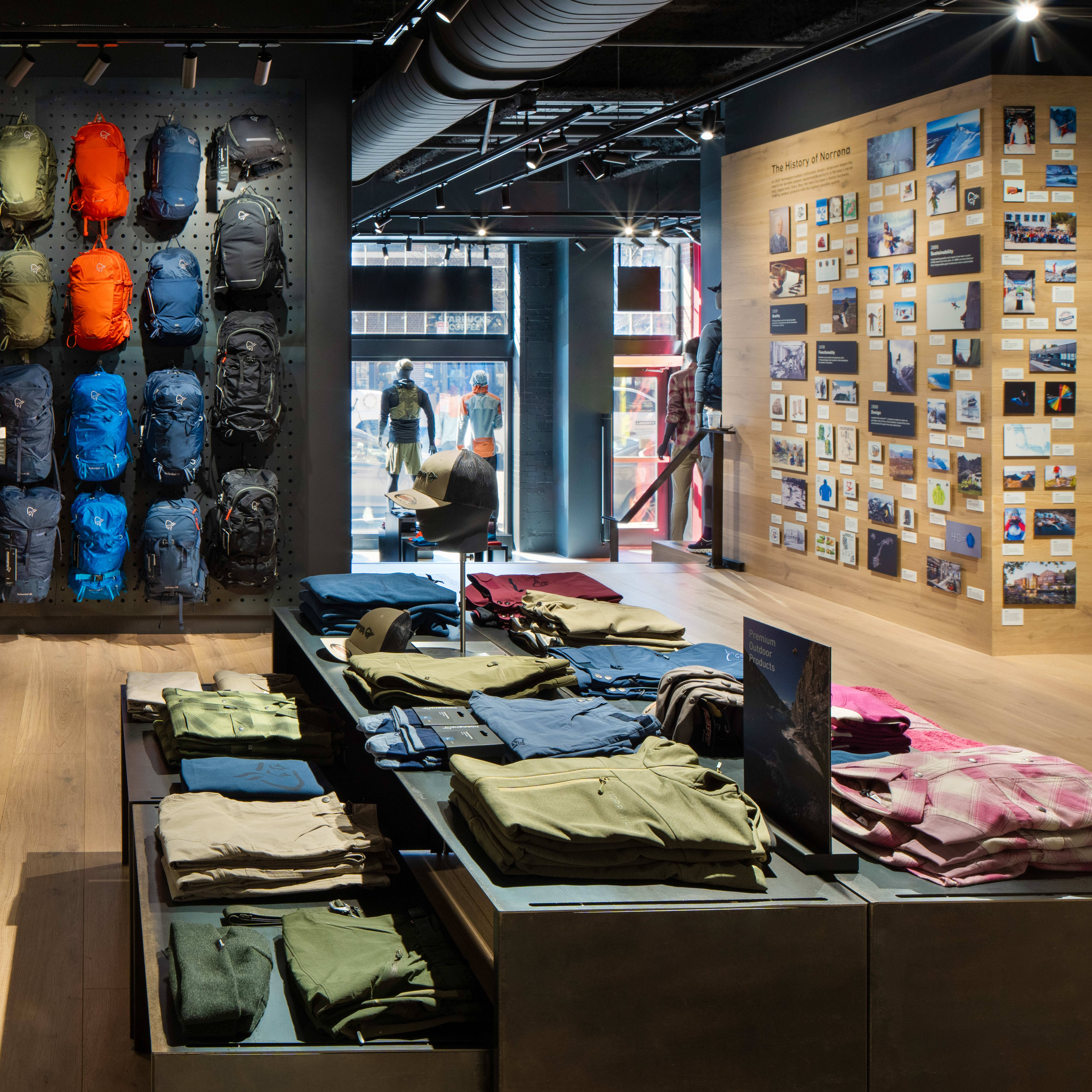 Norrøna backpacks displayed on a wall in a store, along with clothing and hats, in a retail setting.