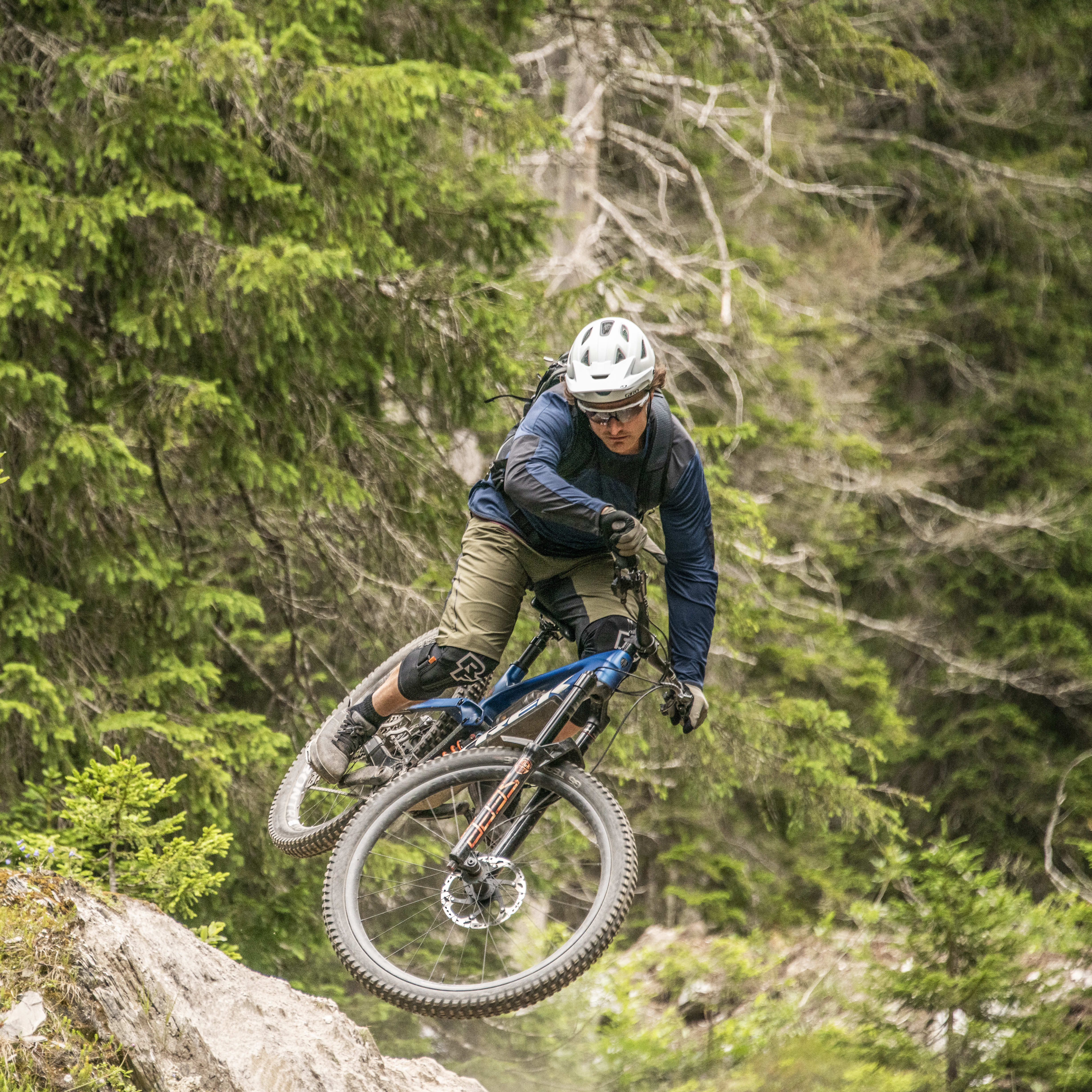 A man wearing a Norrøna outfit is riding a mountain bike through a forest.
