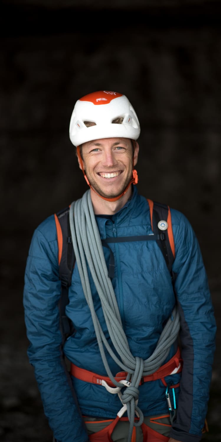 Smiling climber in Norrøna jacket, harness, rope, and Petzl helmet.
