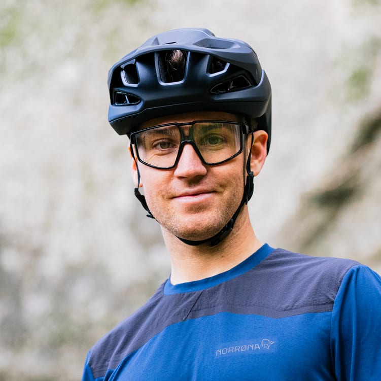 Man wearing a Norrøna shirt, a black helmet, and glasses. He is smiling at the camera.