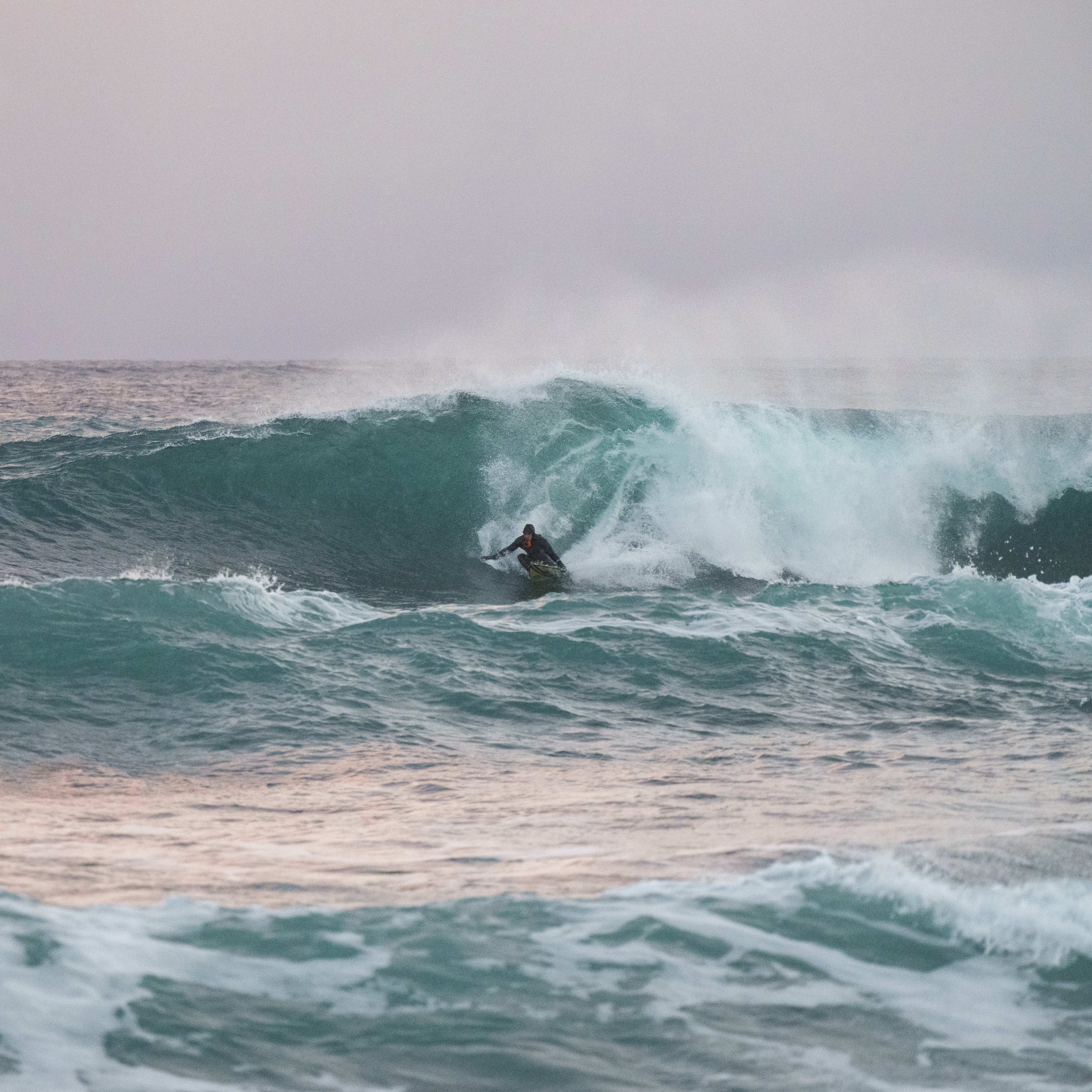 Surfer in a Norrøna wetsuit riding a large turquoise wave.