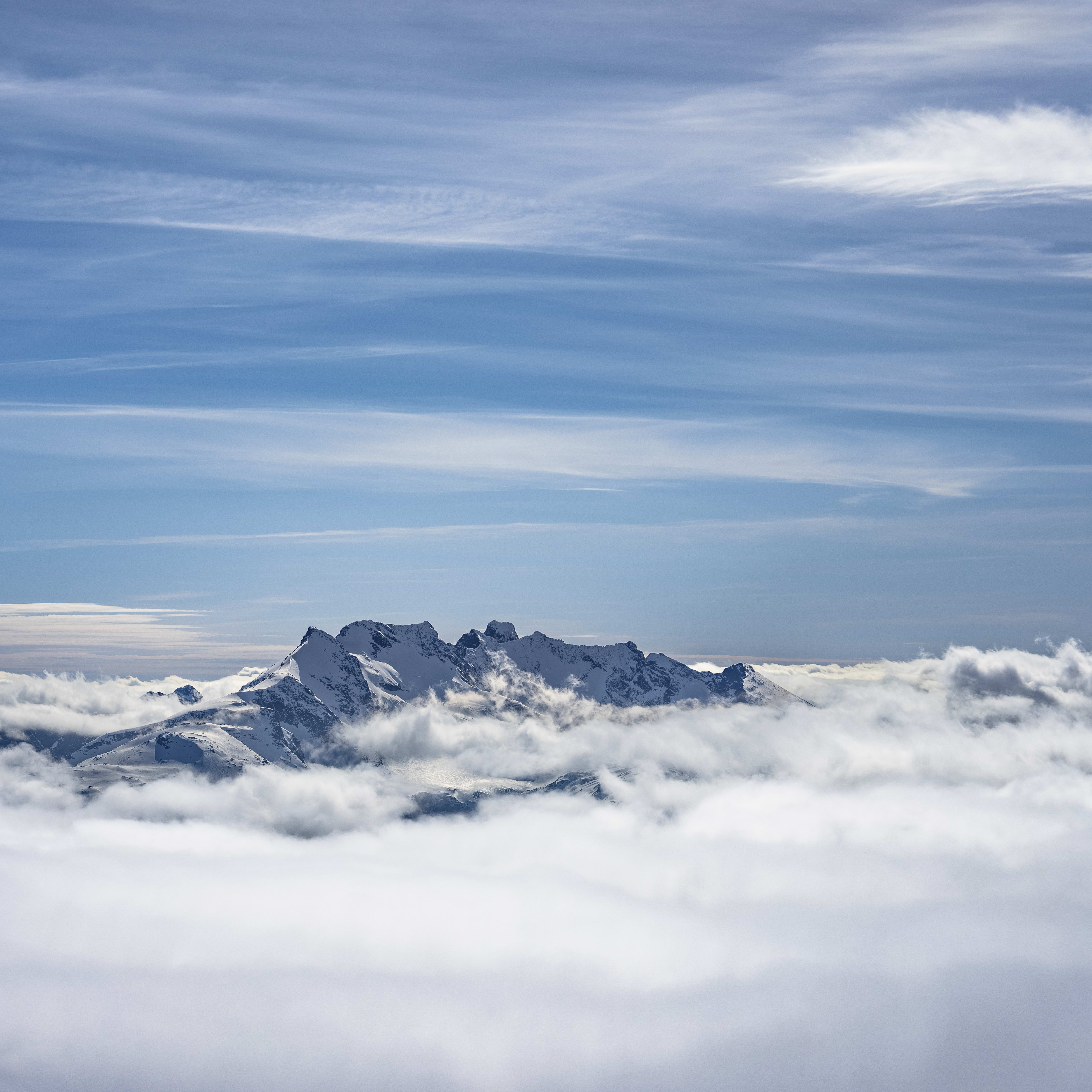 A snow-capped mountain range peeks through a sea of fluffy white clouds against a clear blue sky. 
